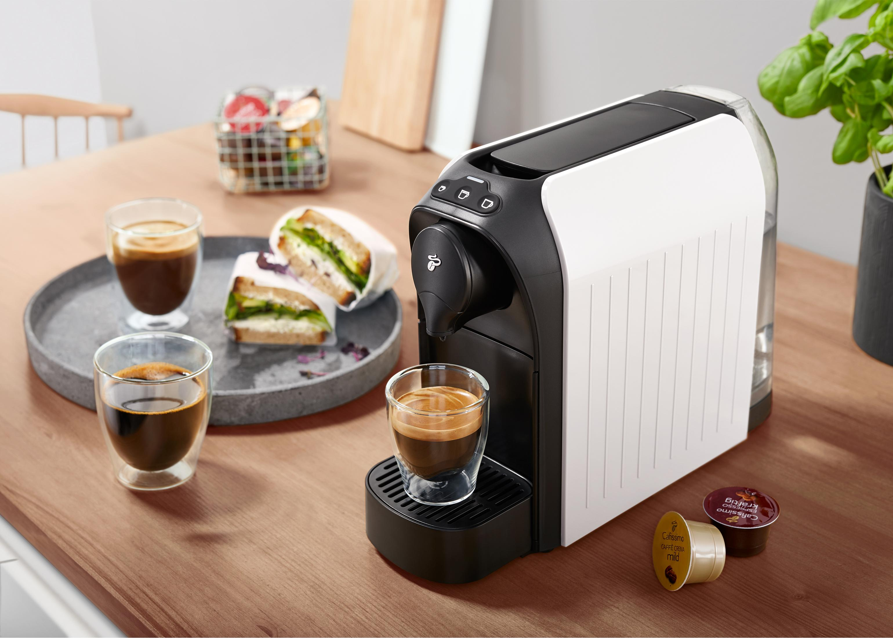 Kaffeemaschine mit zwei Tassen Kaffee und etwas Essen. Es gibt Kaffeepads.