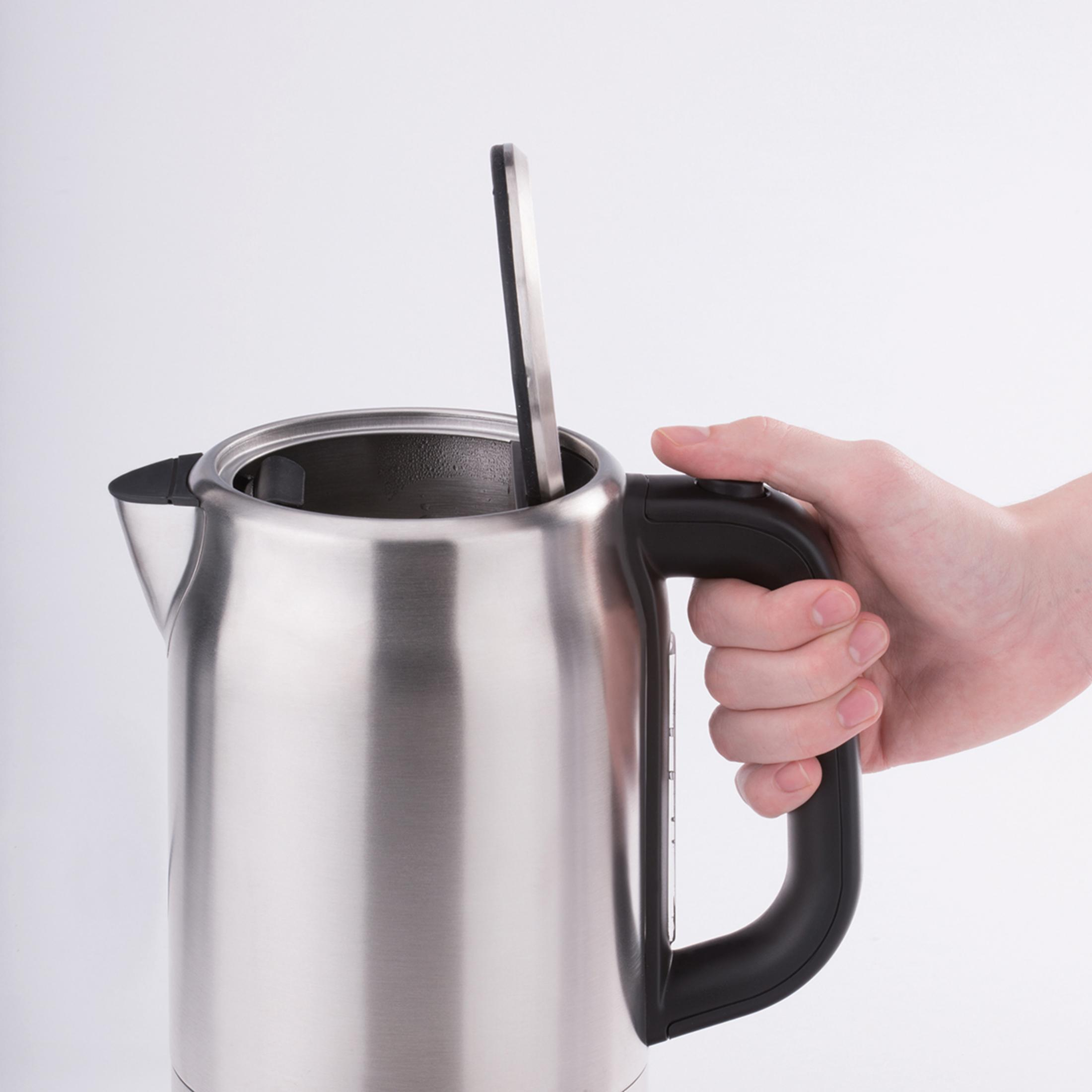 Dłoń trzymająca czarny uchwyt czajnika ze stali nierdzewnej, z łyżką w środku.