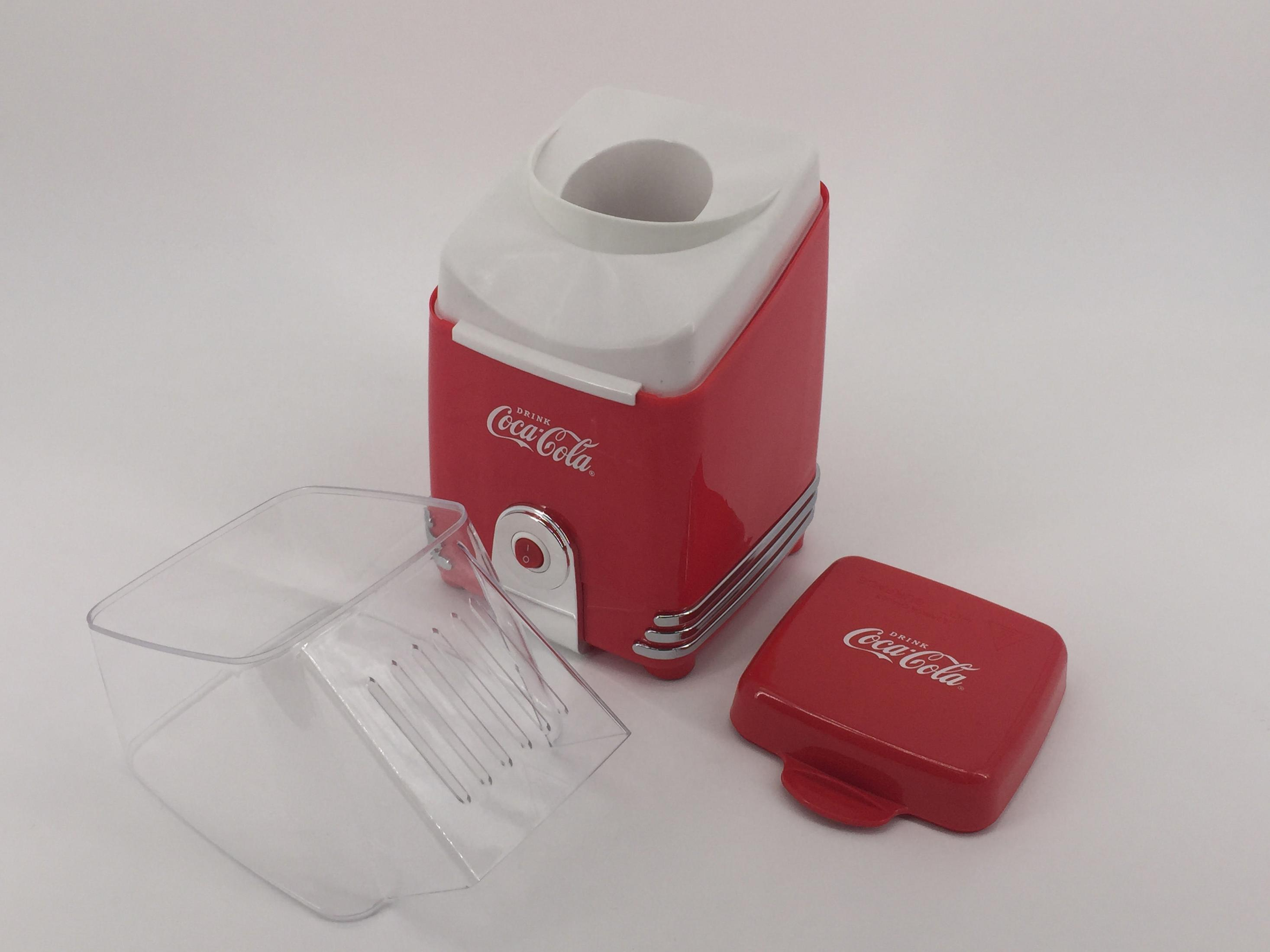 Ein rot-weißer Coca-Cola Popcorn-Maker mit offenem Deckel und Behälter auf weißer Oberfläche.
