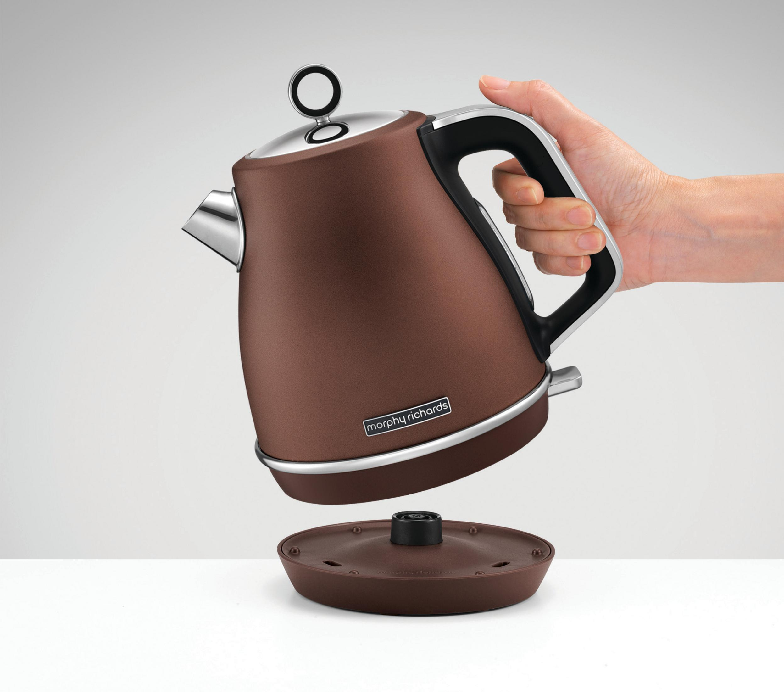 Brązowy czajnik z podstawą i ręką, która go trzyma. To czajnik marki Morphy Richards.