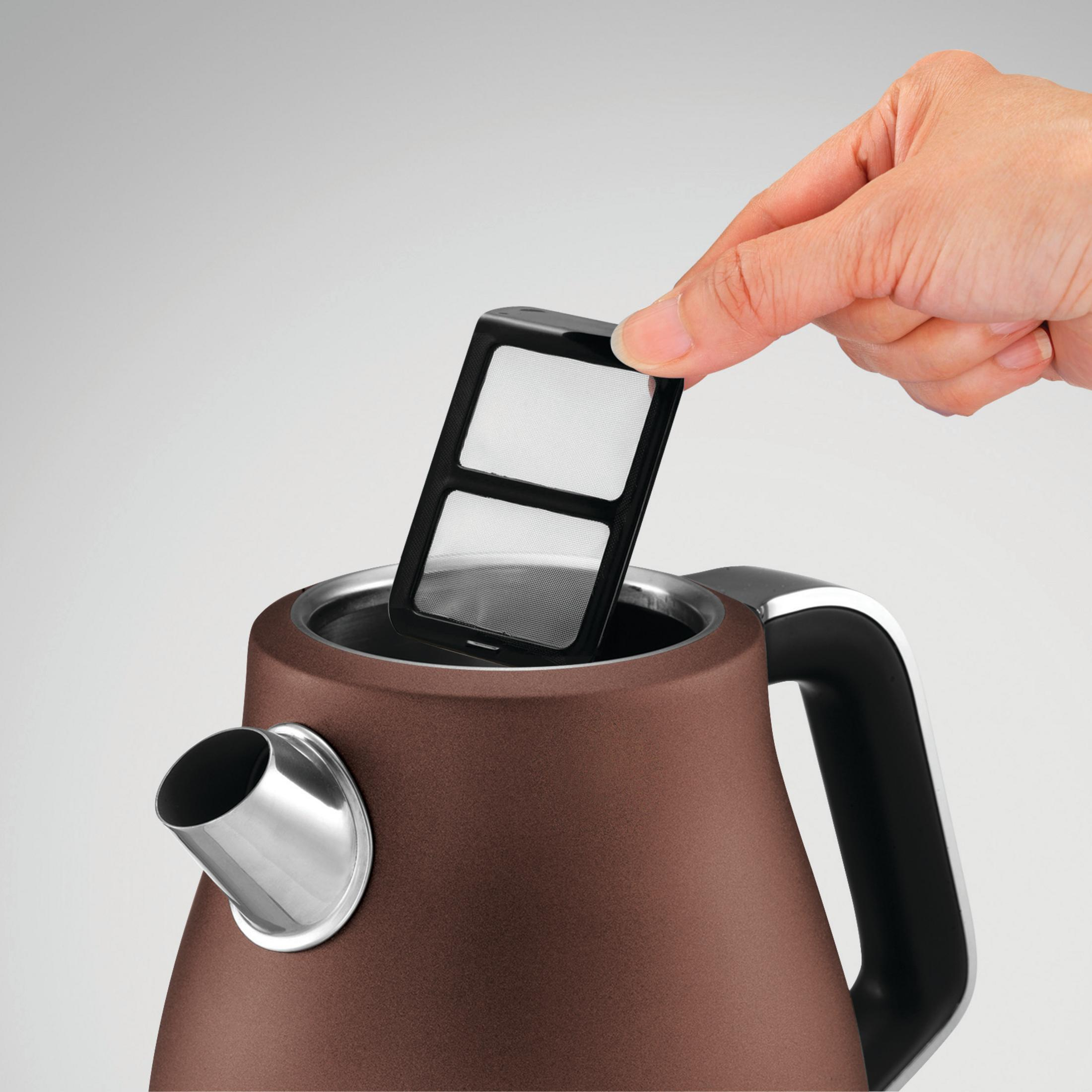 Ręka umieszcza filtr do herbaty w brązowym czajniku. Srebrne akcenty. Białe tło.