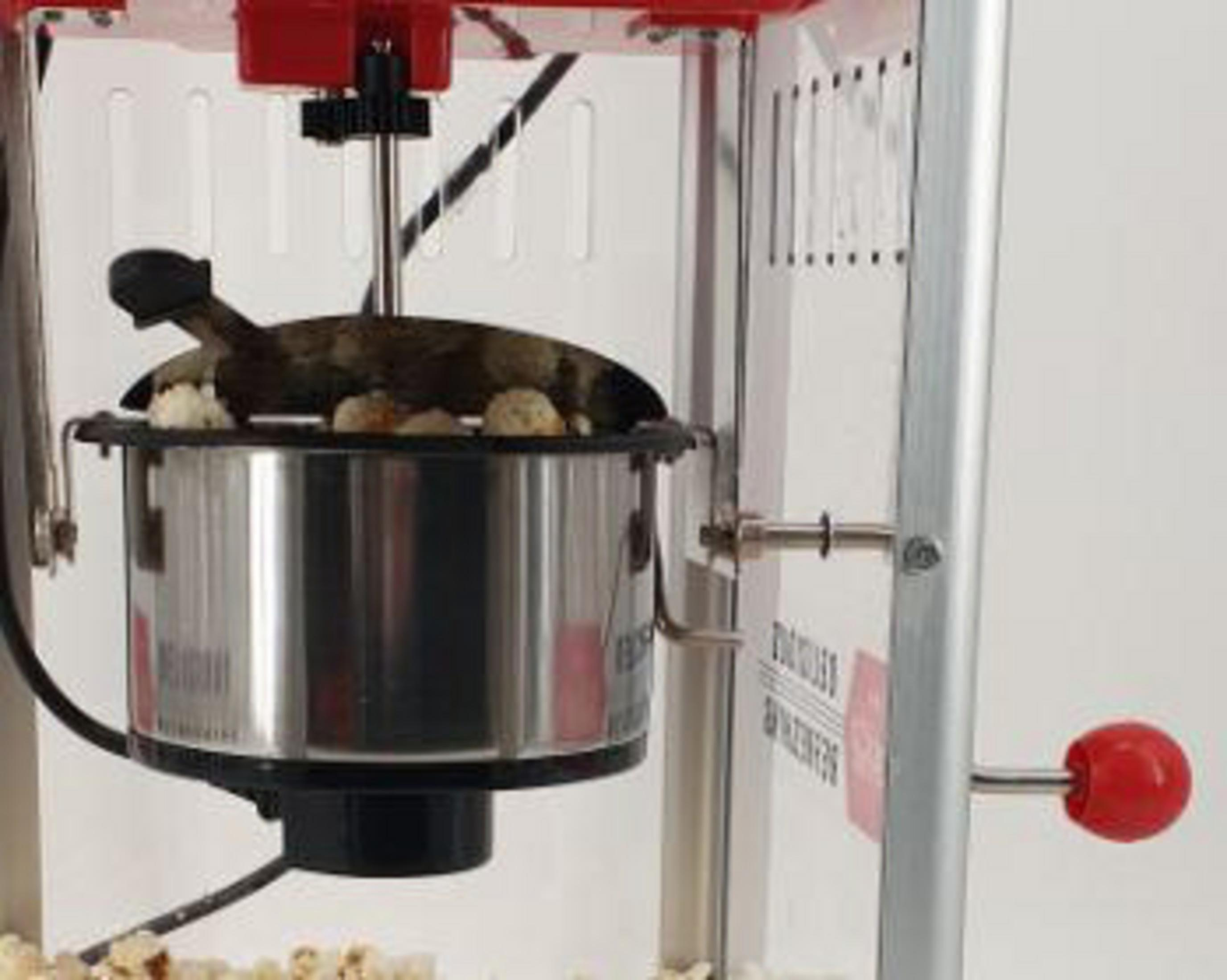 Eine Popcornmaschine mit Edelstahlkessel und rotem Griff, gefüllt mit Popcorn.