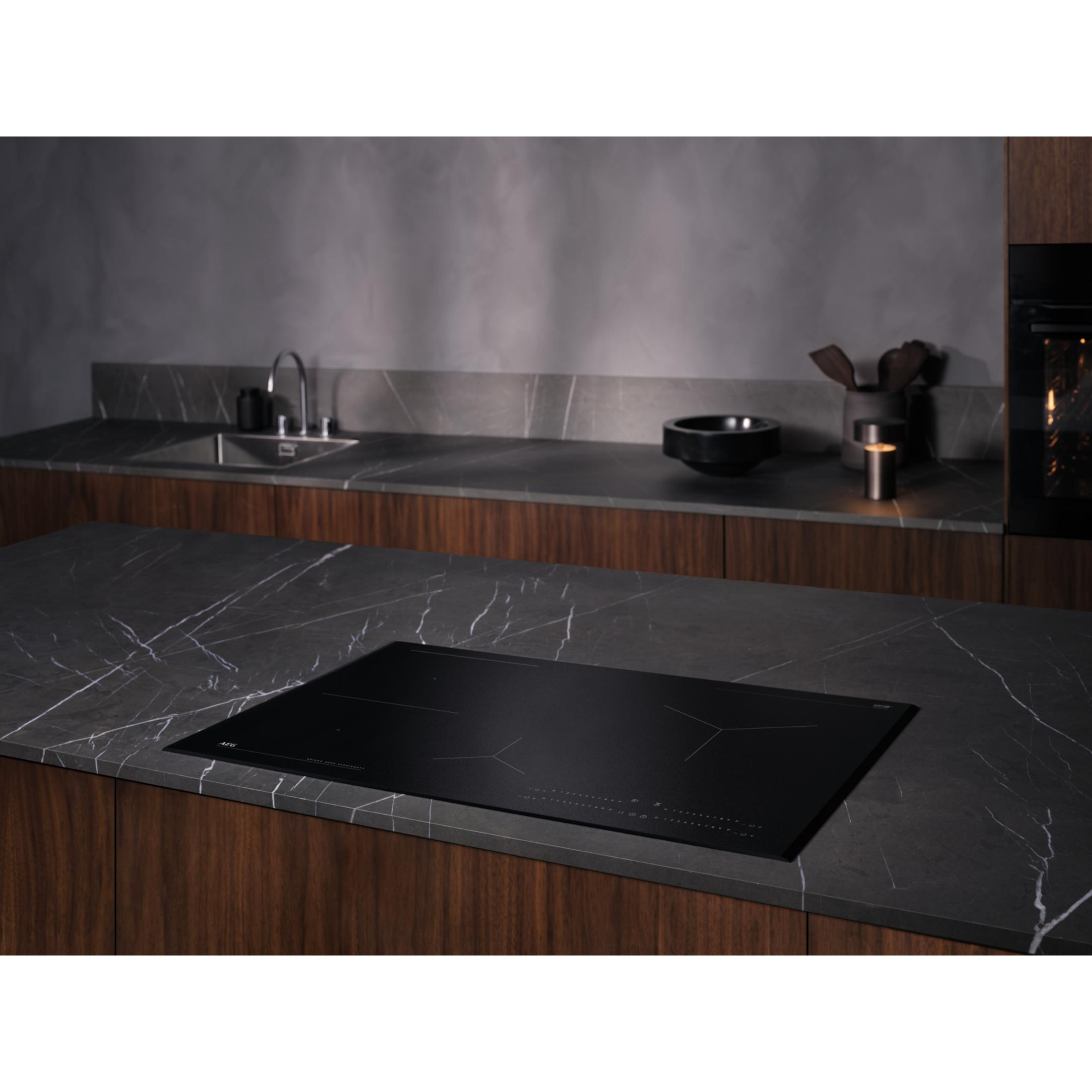 Une table de cuisson à induction noire encastrée dans un comptoir sombre, un évier et des ustensiles de cuisine en arrière-plan.