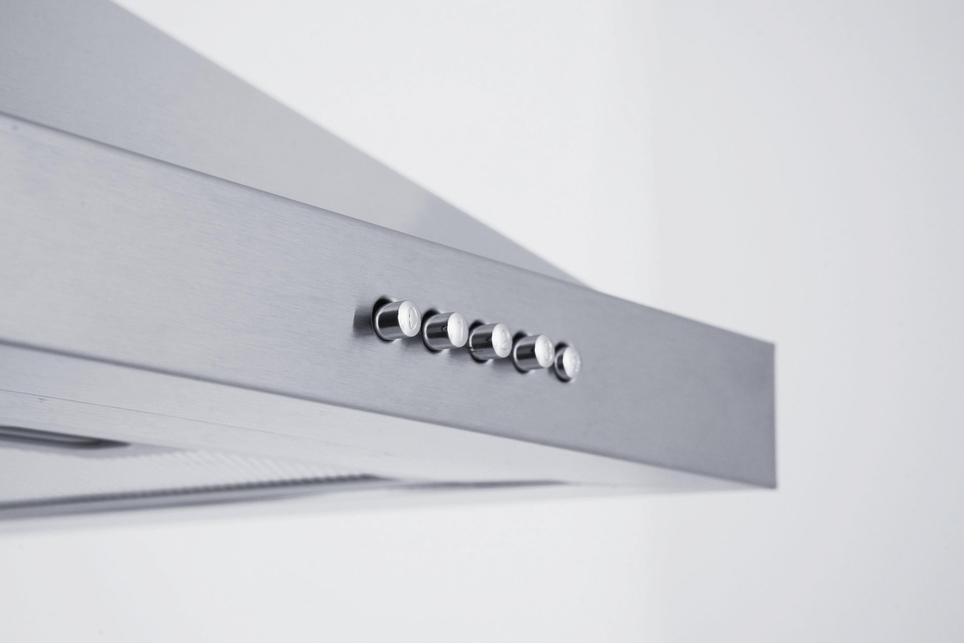 A close-up of a brushed metal range hood with a series of silver buttons on its front edge.