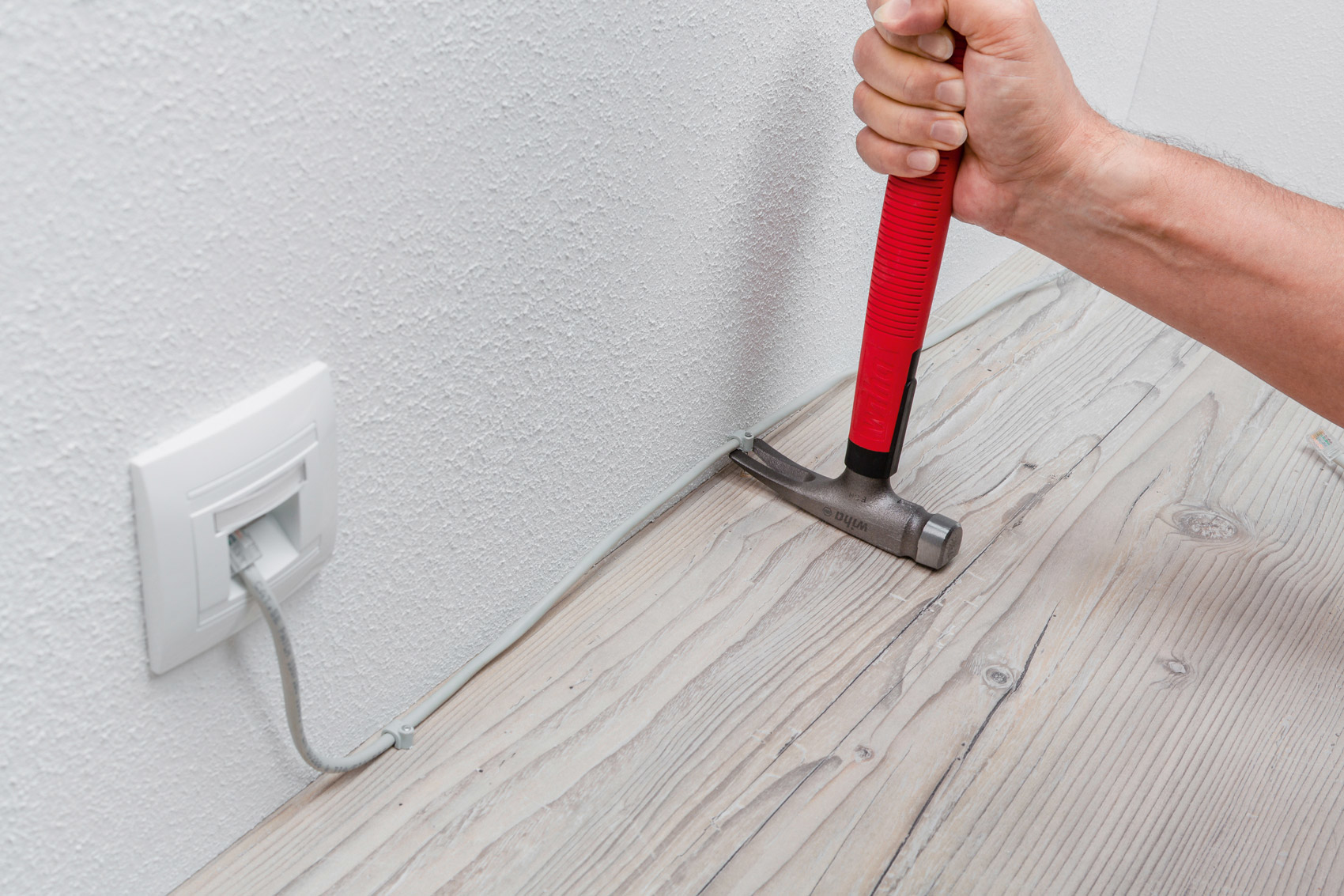 Martillo golpeando un clavo cerca de una pared con un cable, en un suelo de madera.