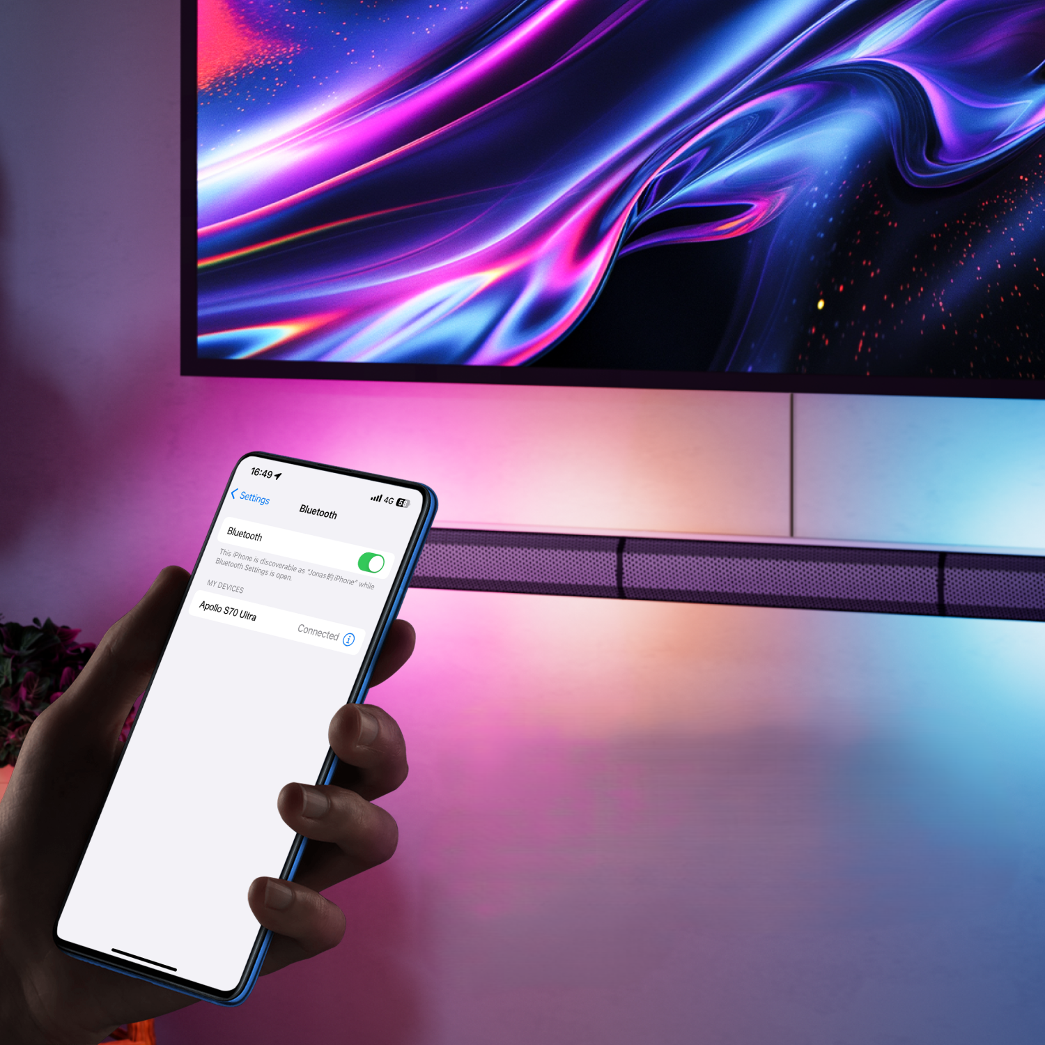 Dłoń trzymająca podłączony smartfon do telewizora i soundbaru z połączeniem bluetooth.
