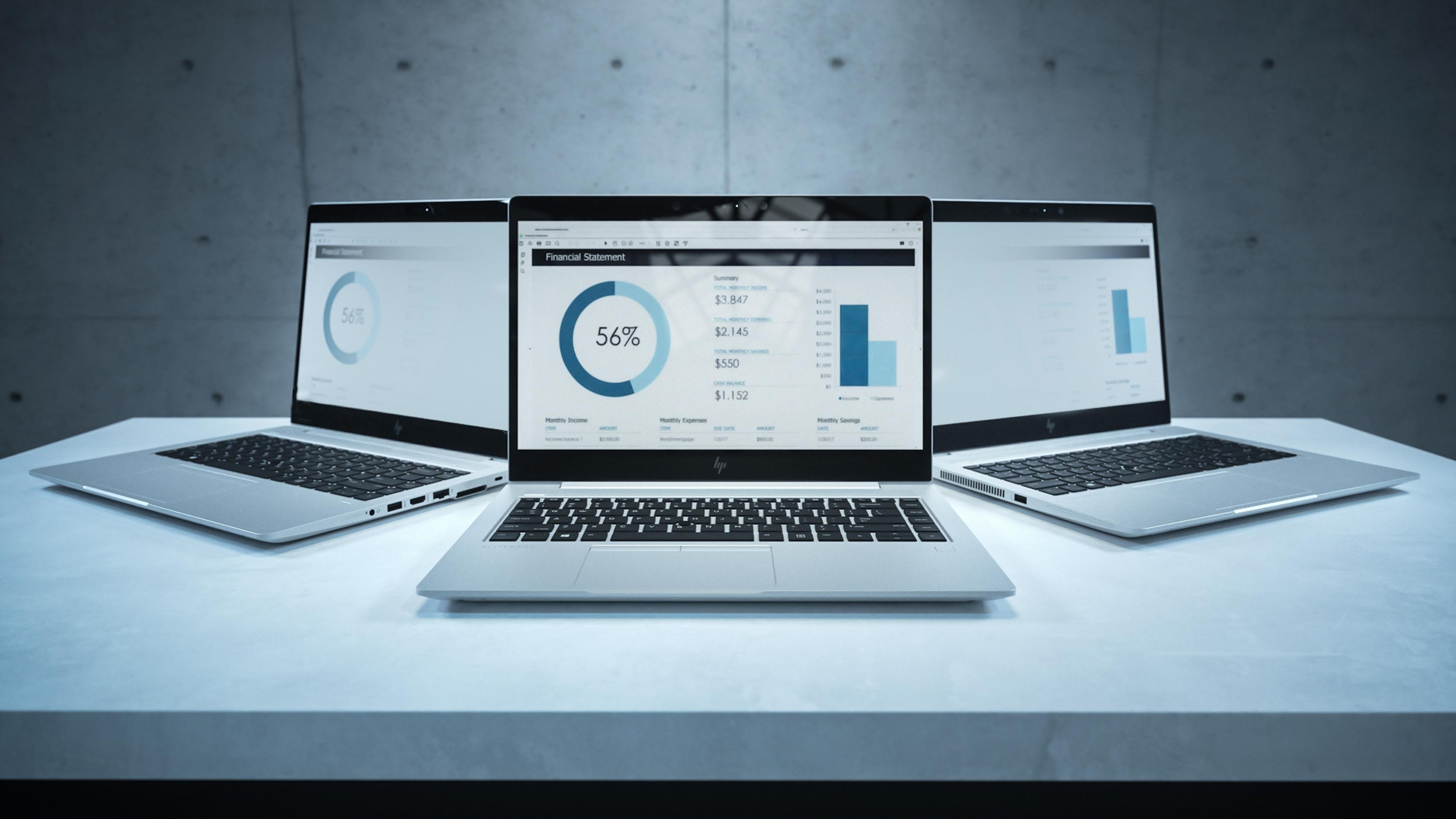 Drei Laptops auf einer Oberfläche mit Finanzbericht, Diagrammen und Zahlen.