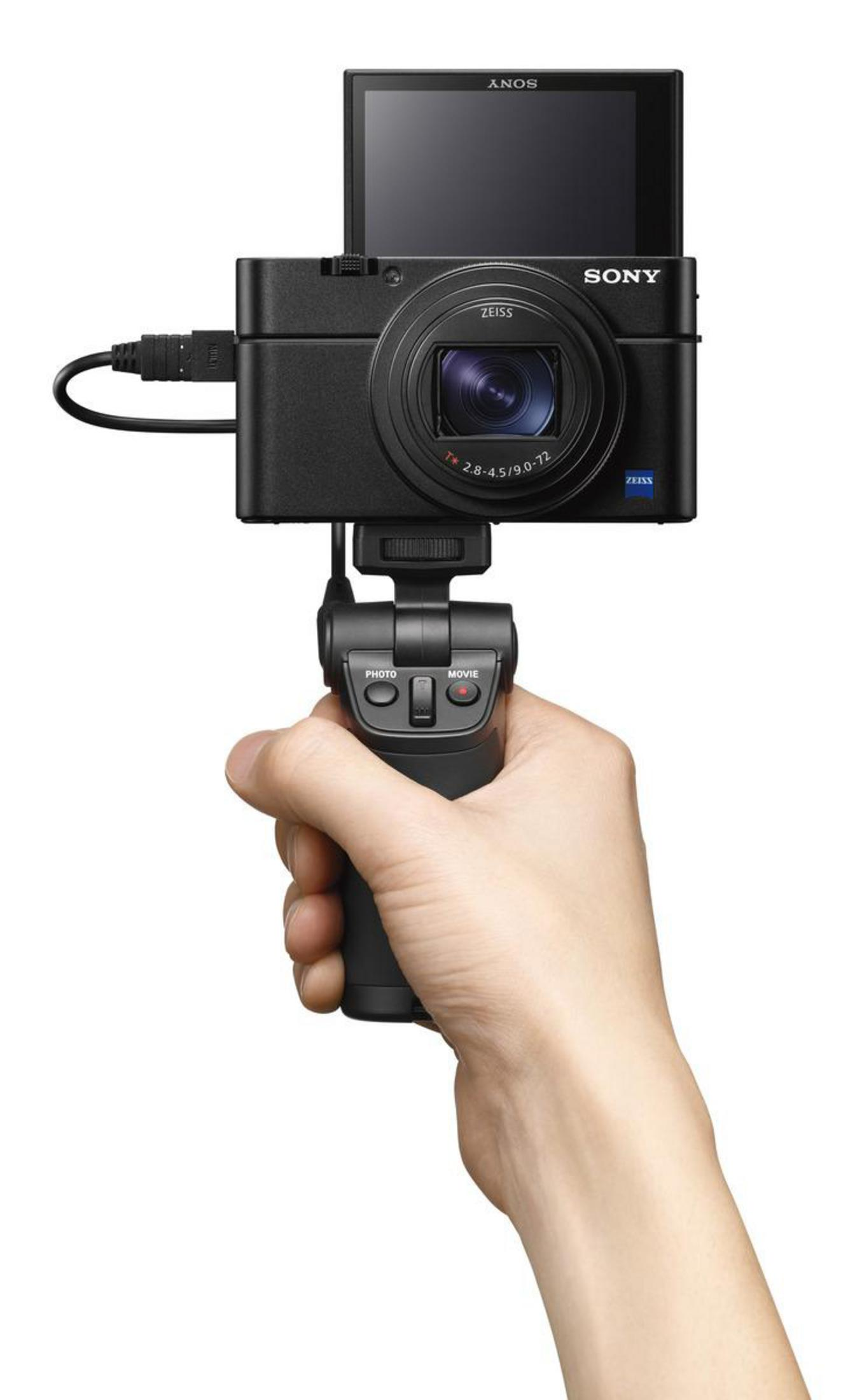 Dłoń trzymająca czarny aparat Sony z ekranem i uchwytem. Białe tło.