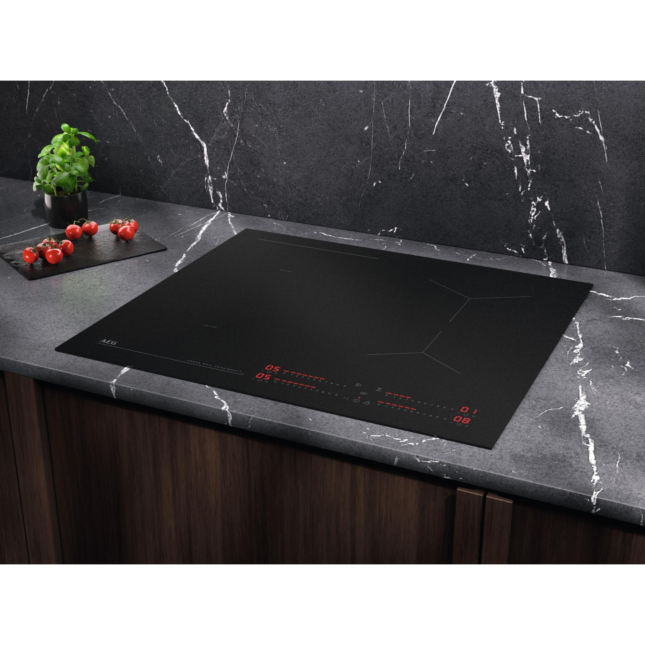 Table de cuisson à induction noire sur un comptoir. Petites plantes et tomates visibles.