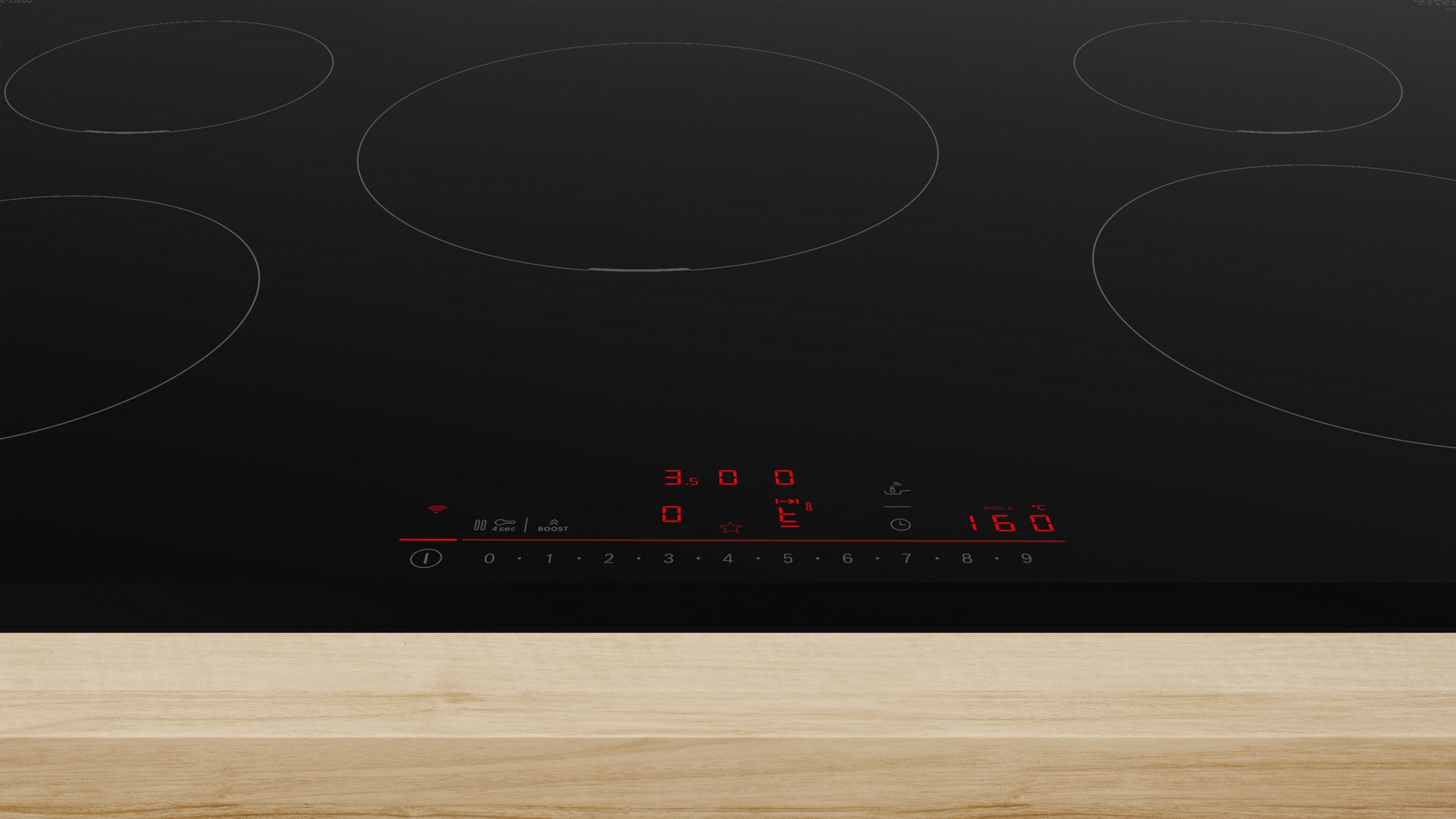 Piano cottura in vetroceramica nero con pannello comandi, su superficie in legno. Vista da vicino, display chiaro.