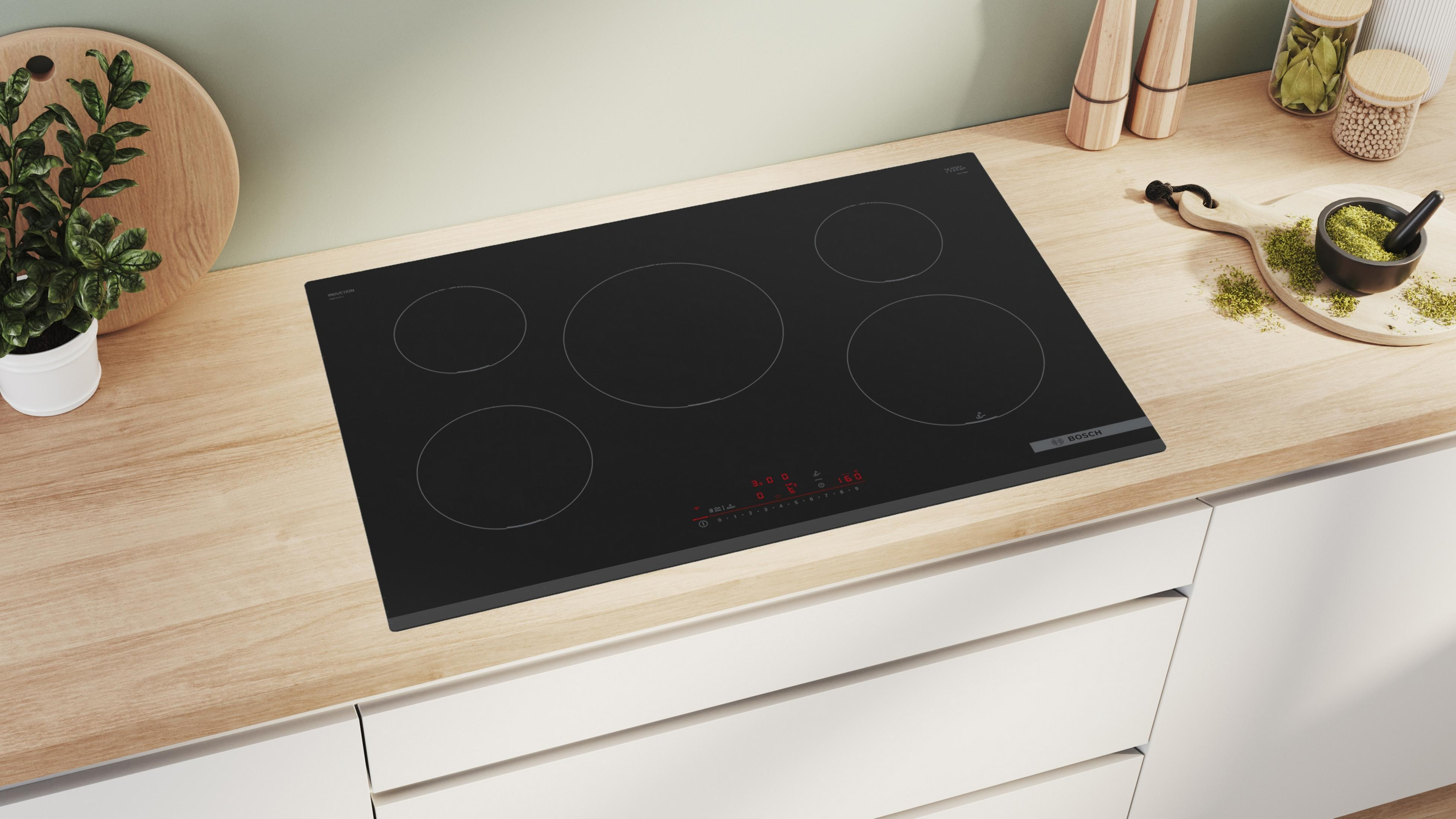 Piano cottura in vetroceramica nero con quattro fuochi e pannello comandi, su un piano di lavoro in legno in cucina.