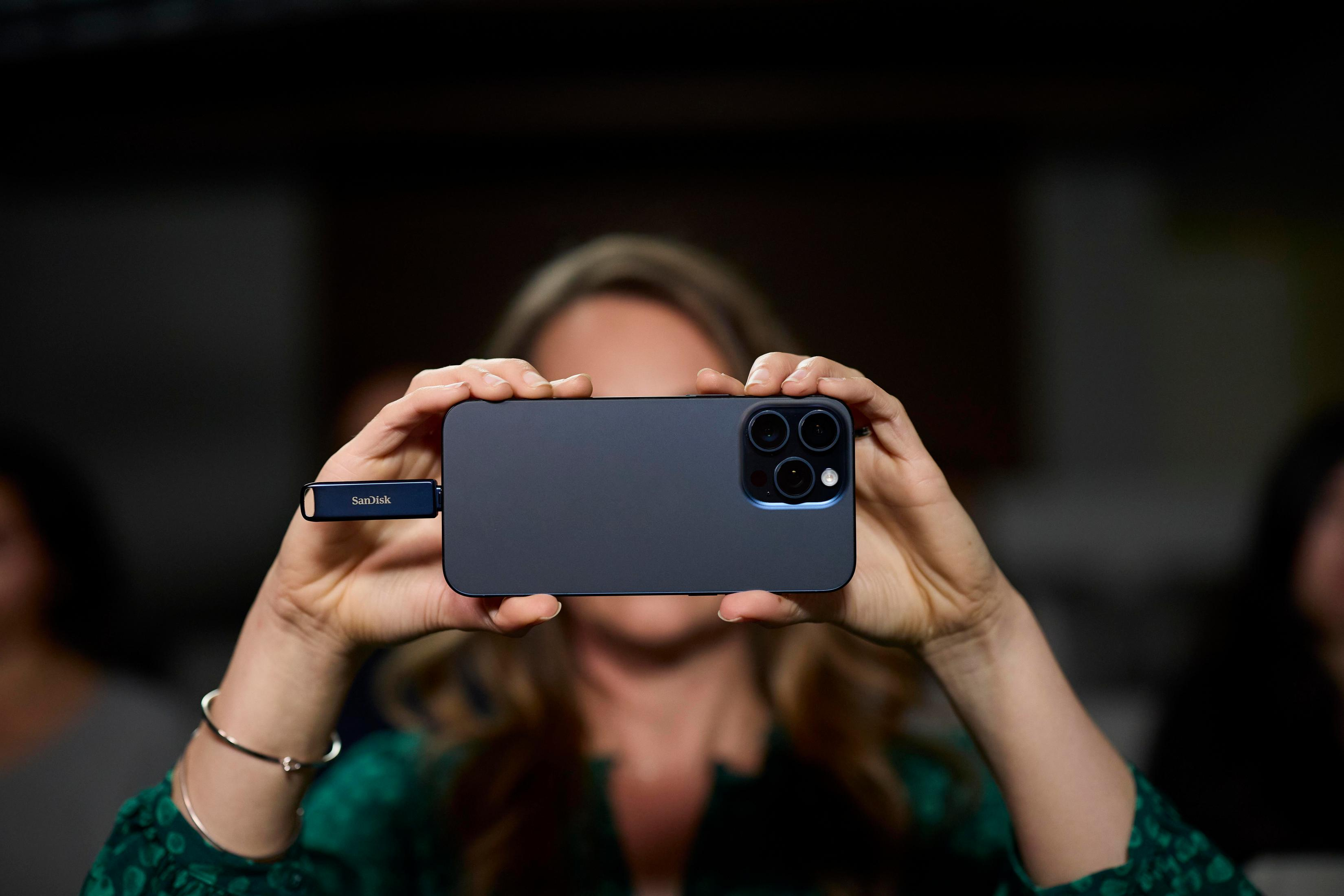 Personne tenant un téléphone avec une clé USB bleue attachée, devant un fond flou.