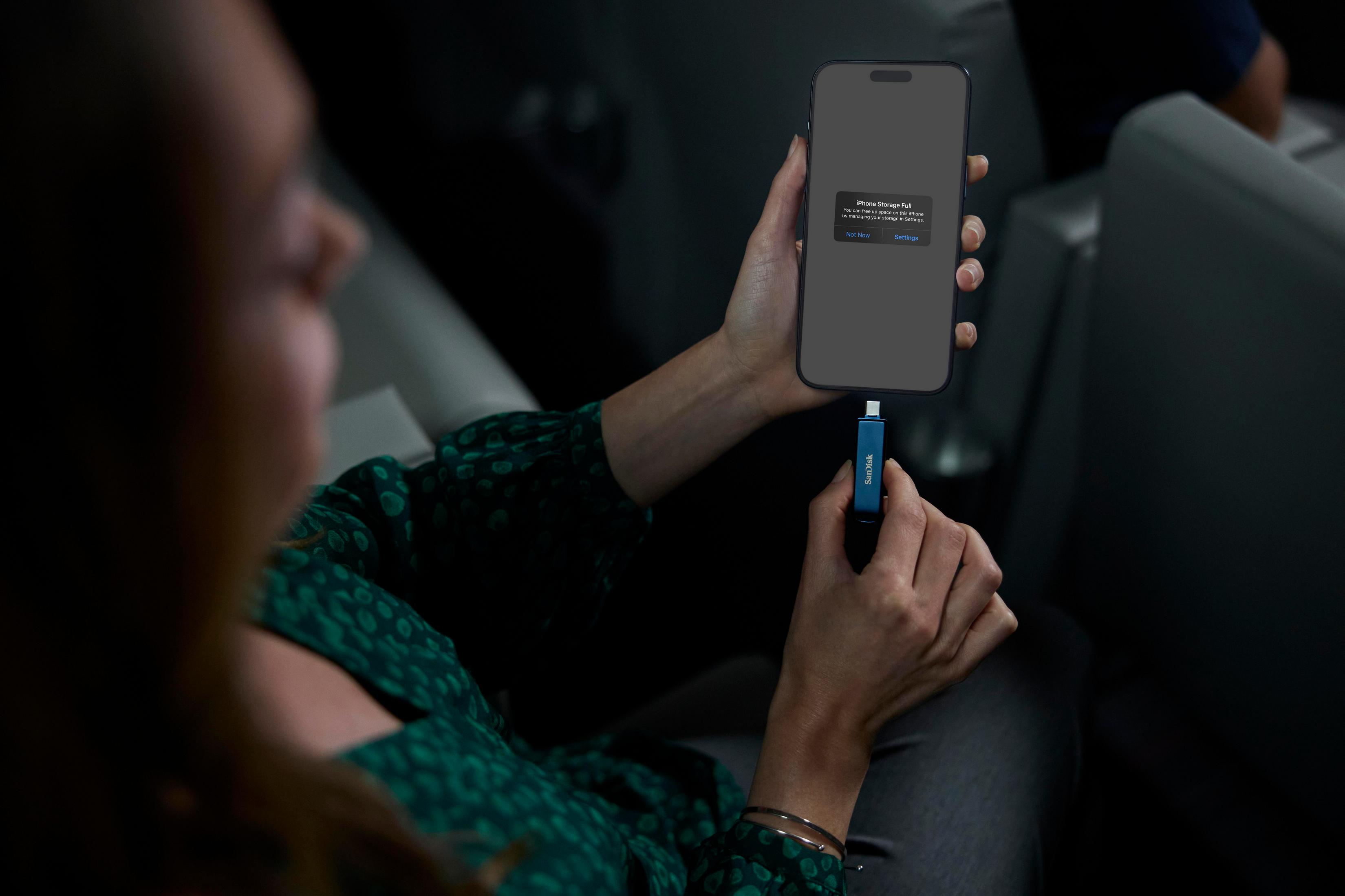 Femme tenant un téléphone avec le message 'Phone Storage Full' et un adaptateur USB-C bleu connecté.