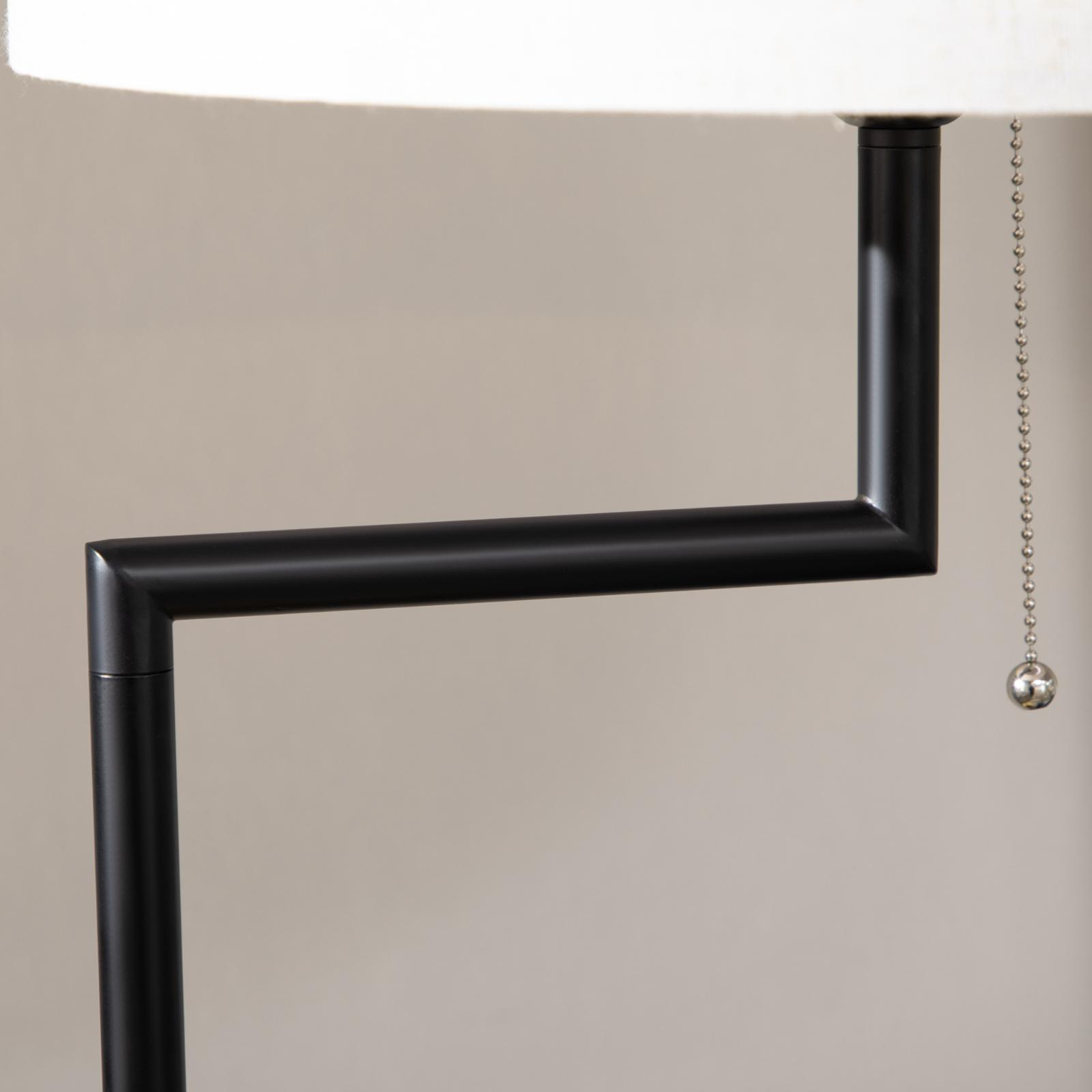 Schwarze Lampe mit weißem Schirm und Zugkette. Der Hintergrund ist eine neutrale Wand.