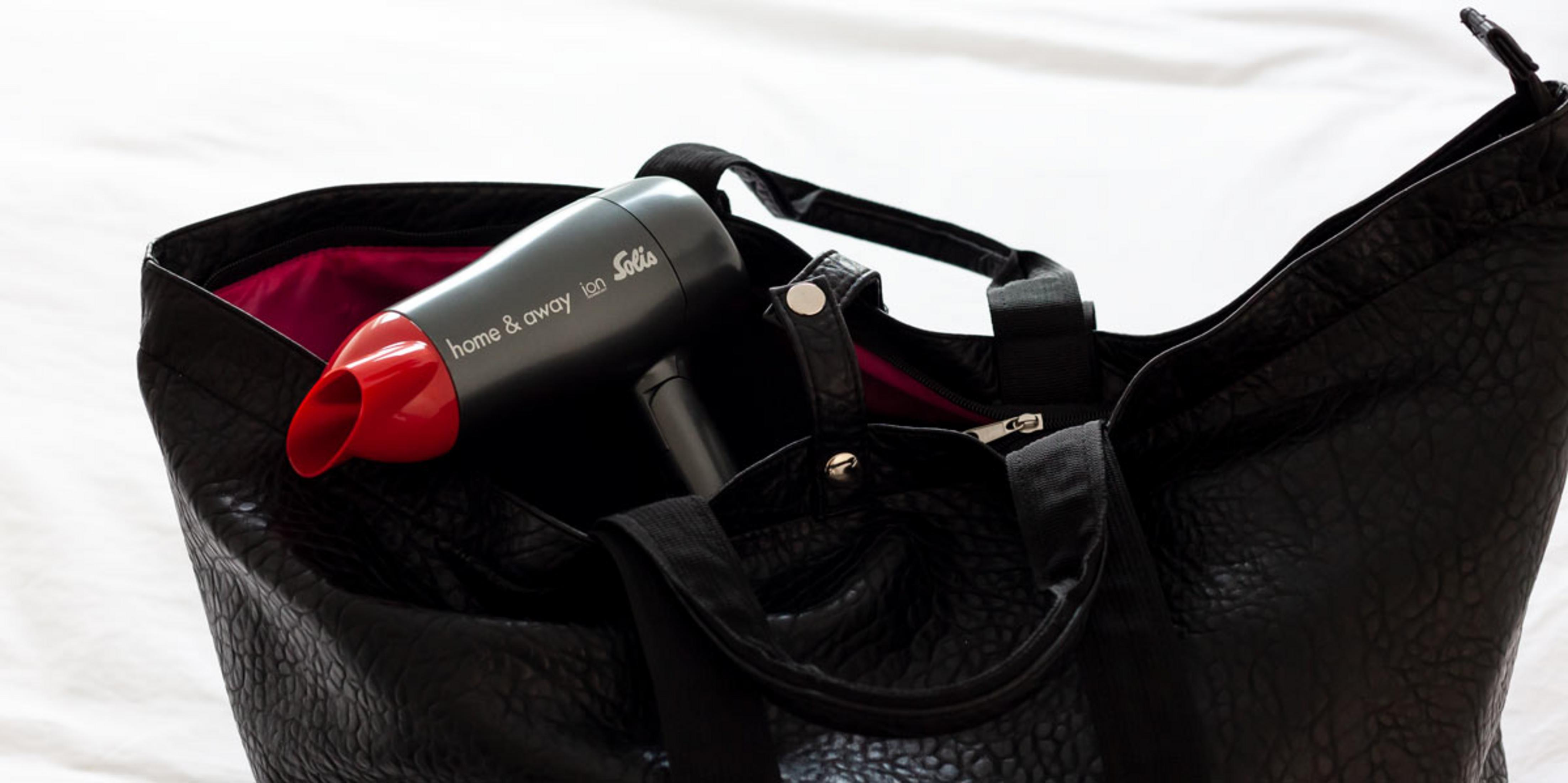 Czarna torba z czerwoną i czarną suszarką do włosów w środku. Torba leży na białej powierzchni.