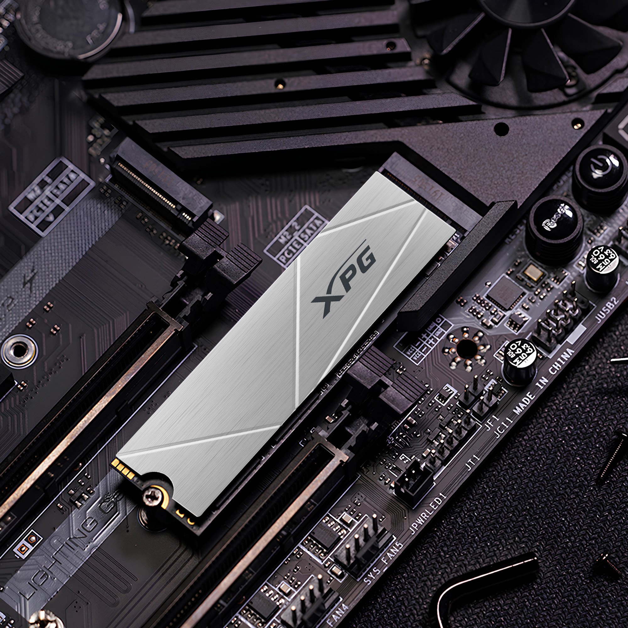 Dysk SSD XPG zainstalowany na płycie głównej. Ma metalowe wykończenie. Płyta główna jest czarna.