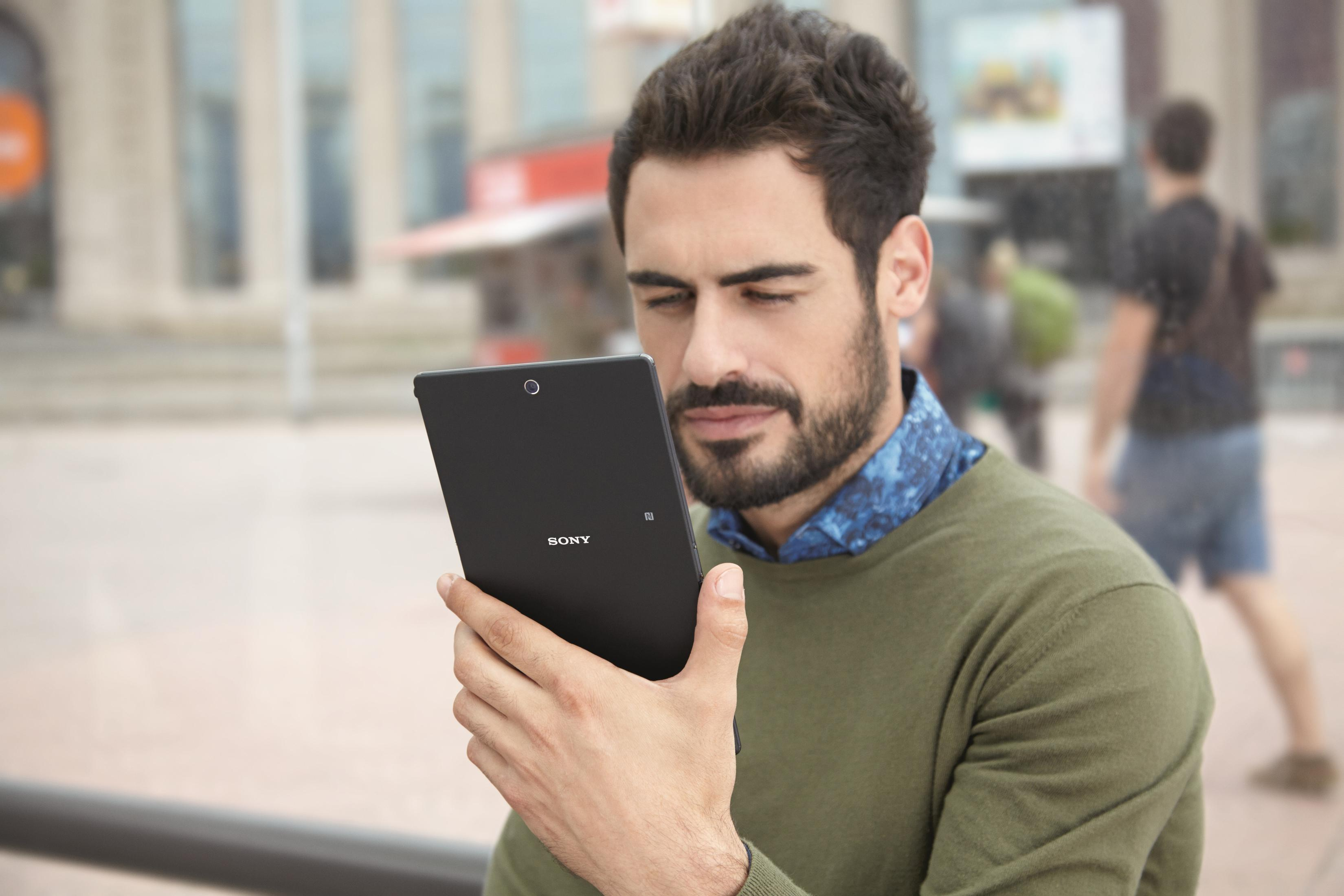 Mann hält schwarzes Tablet, schaut darauf. Hintergrund zeigt Stadtansicht.