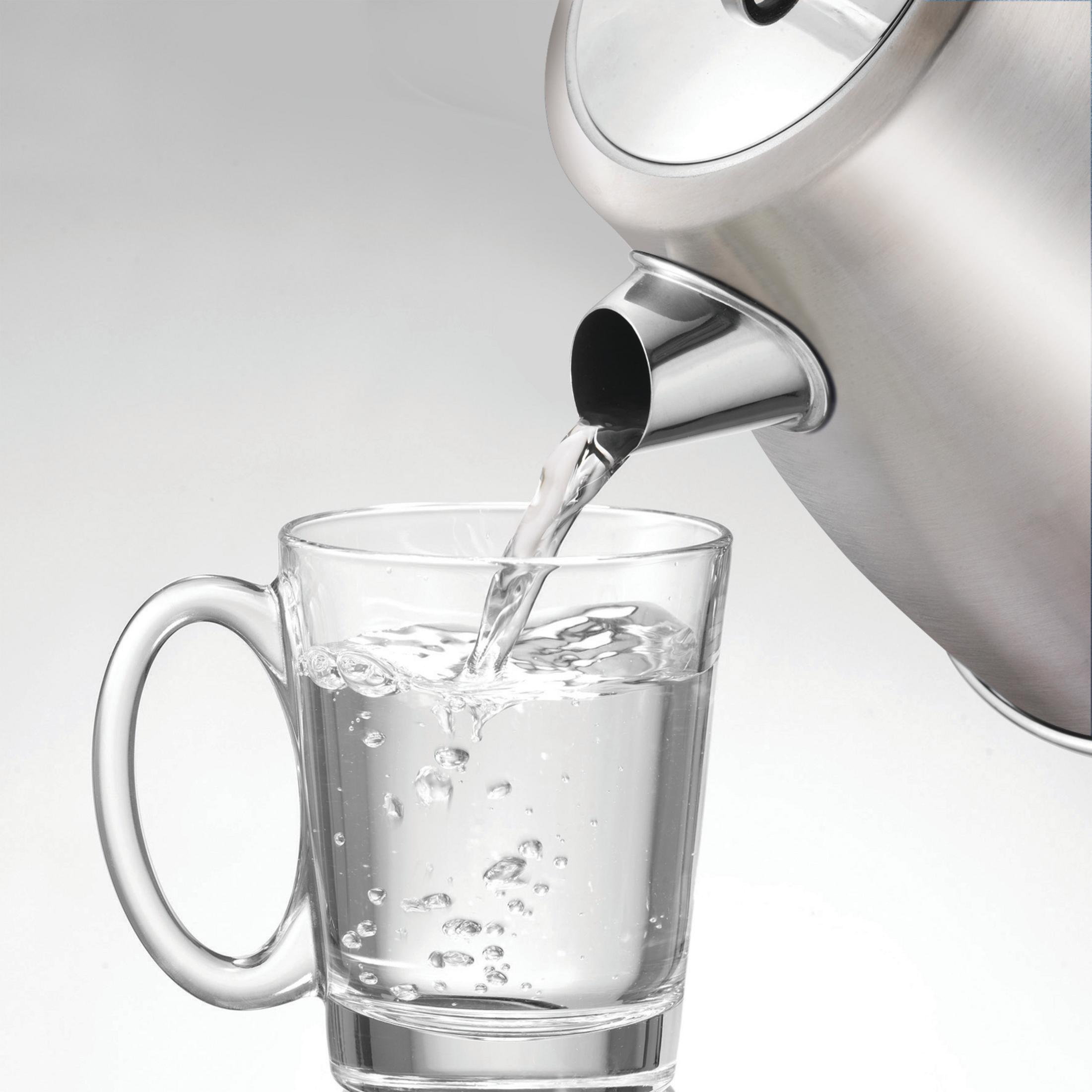 Woda wlewana z czajnika do szklanki. Białe tło.