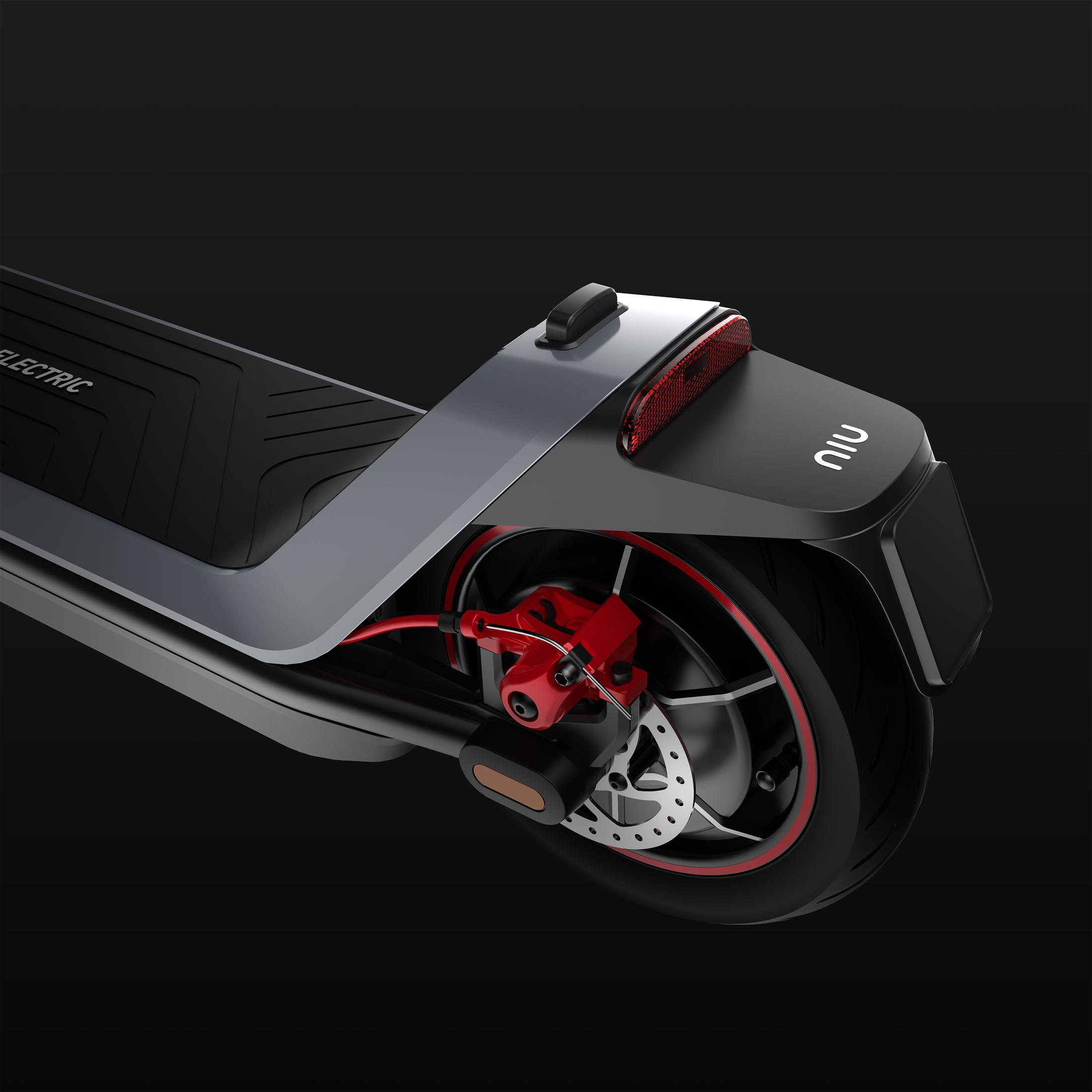 Zbliżenie tylnej części hulajnogi elektrycznej. Czarna opona z czerwonym paskiem, czerwony zacisk hamulcowy i szary błotnik.