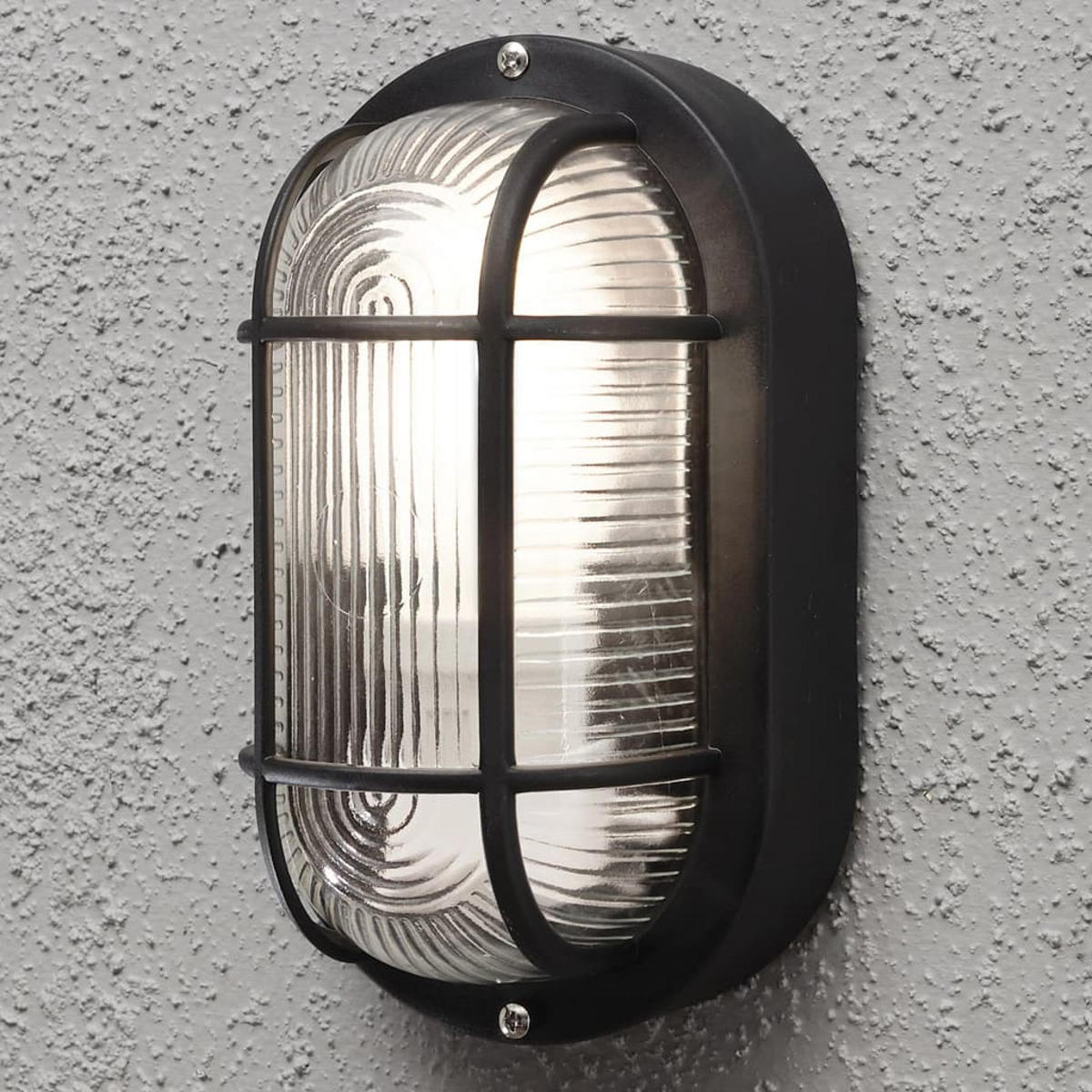 Eine ovale, schwarze Außenleuchte an einer strukturierten grauen Wand. Das Licht ist an.