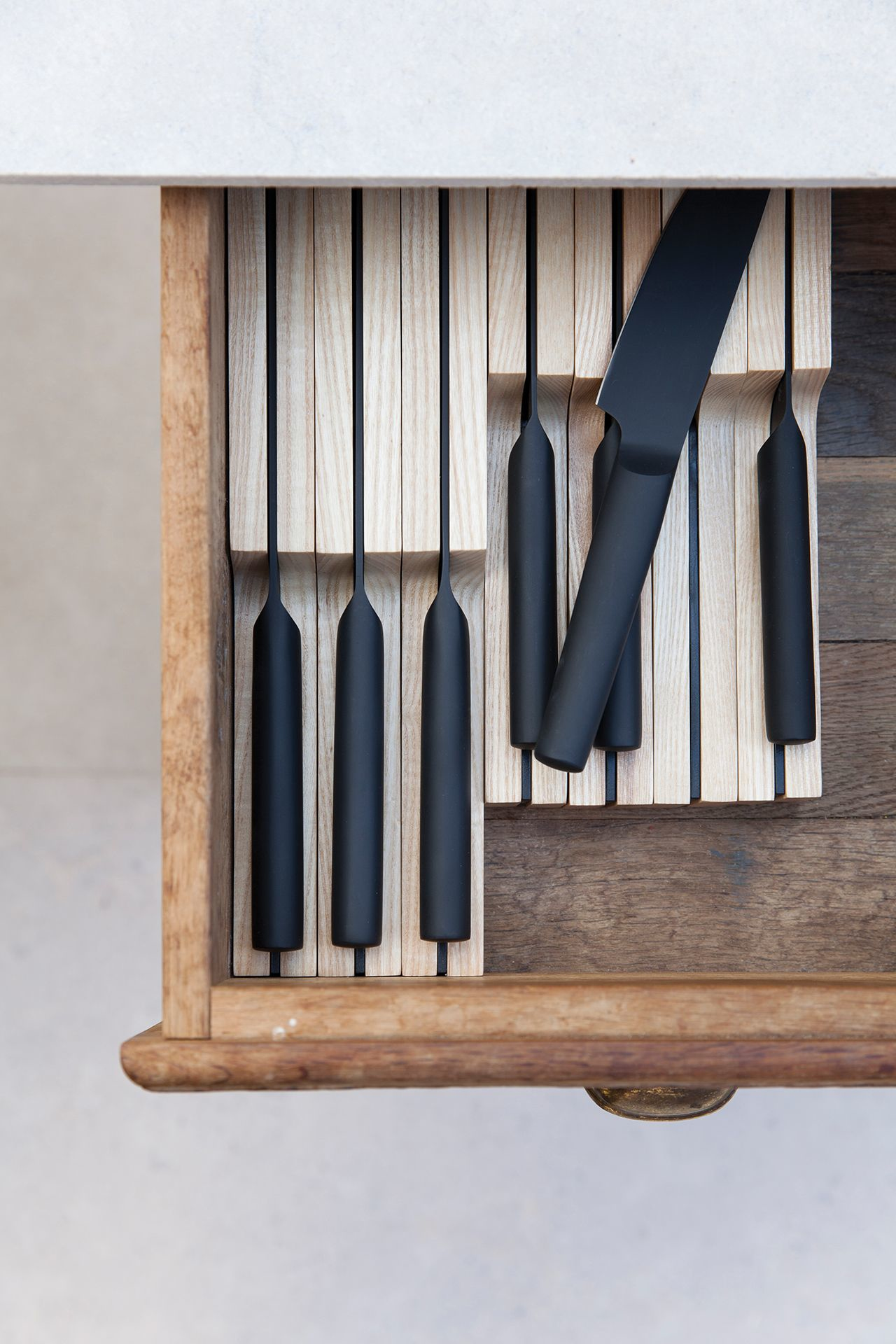 Open drawer with wooden dividers and black knives. One knife is partially out of the divider.