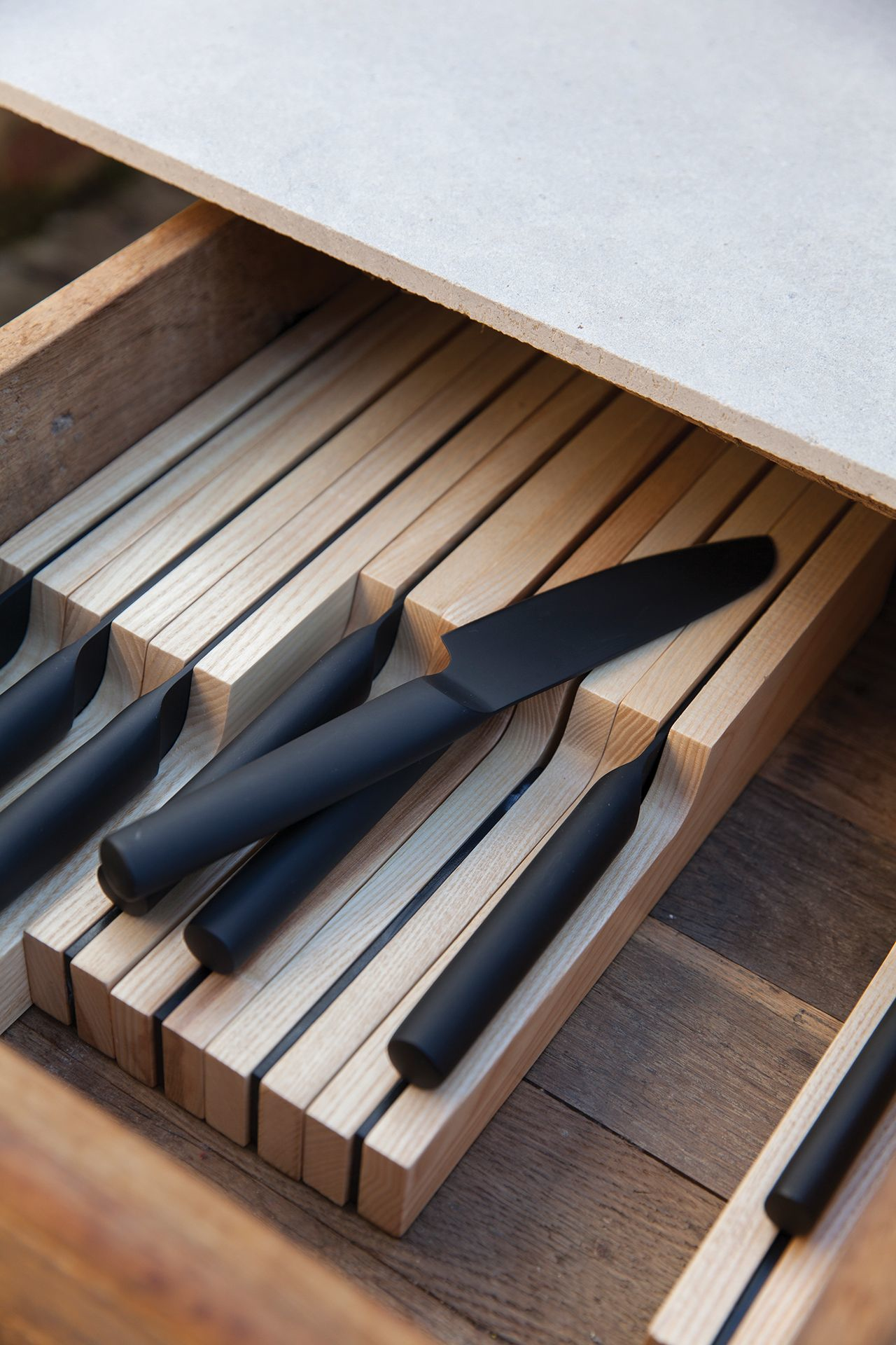 Drawer with wooden dividers holding black knives. Knives are in a drawer.