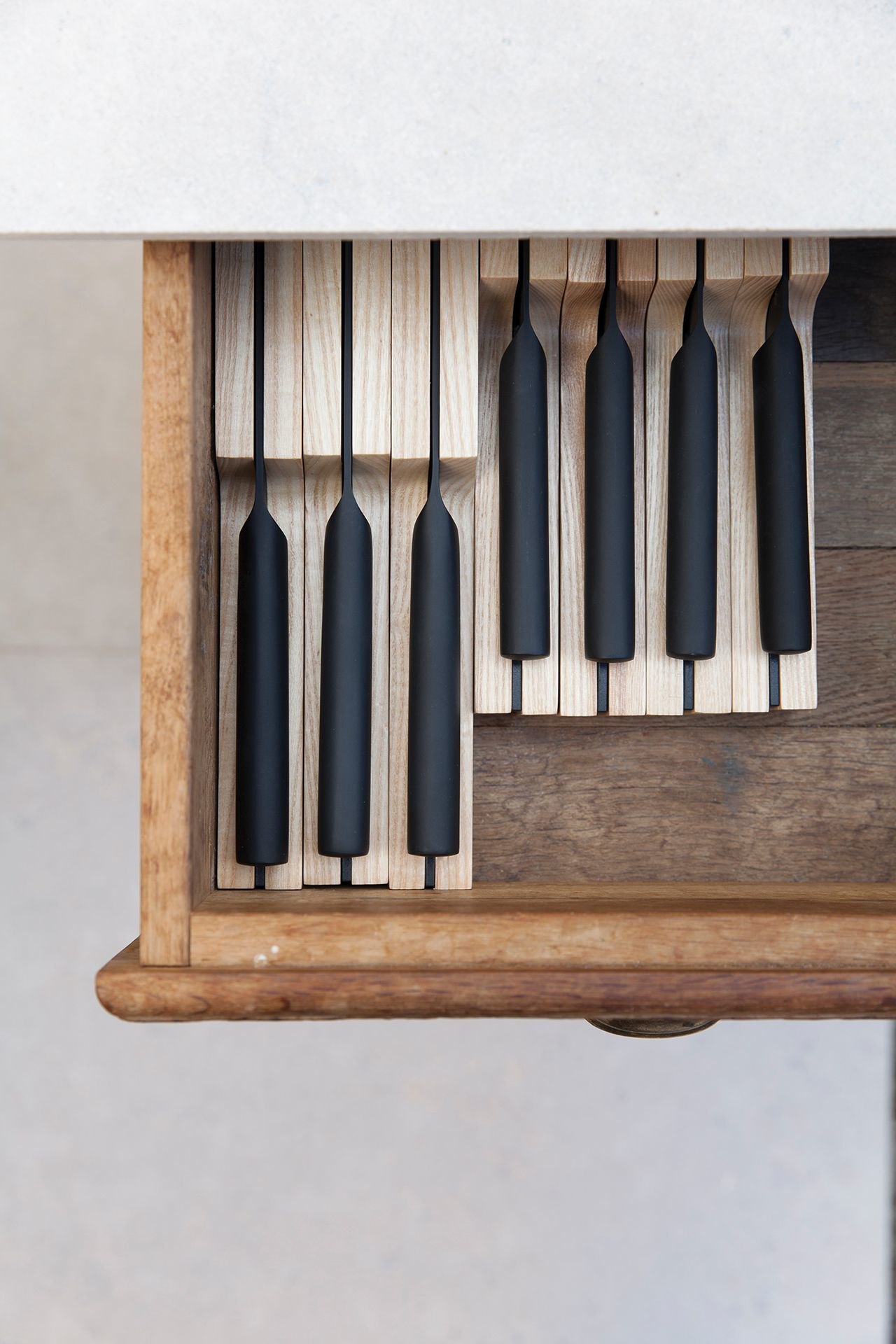 Drawer with wooden dividers holding black knives. Knives arranged neatly.