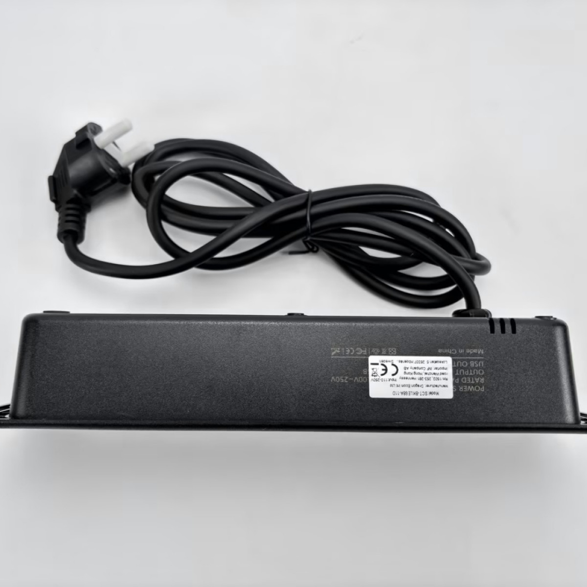 Czarny przedłużacz z czarnym przewodem i białą wtyczką. Tło jest białe.