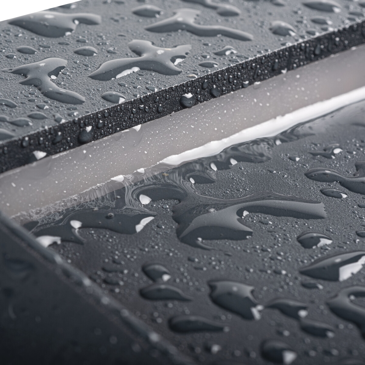 Primer plano de superficie húmeda, gris oscuro con gotas de agua, reflejando la luz. El fondo es blanco.