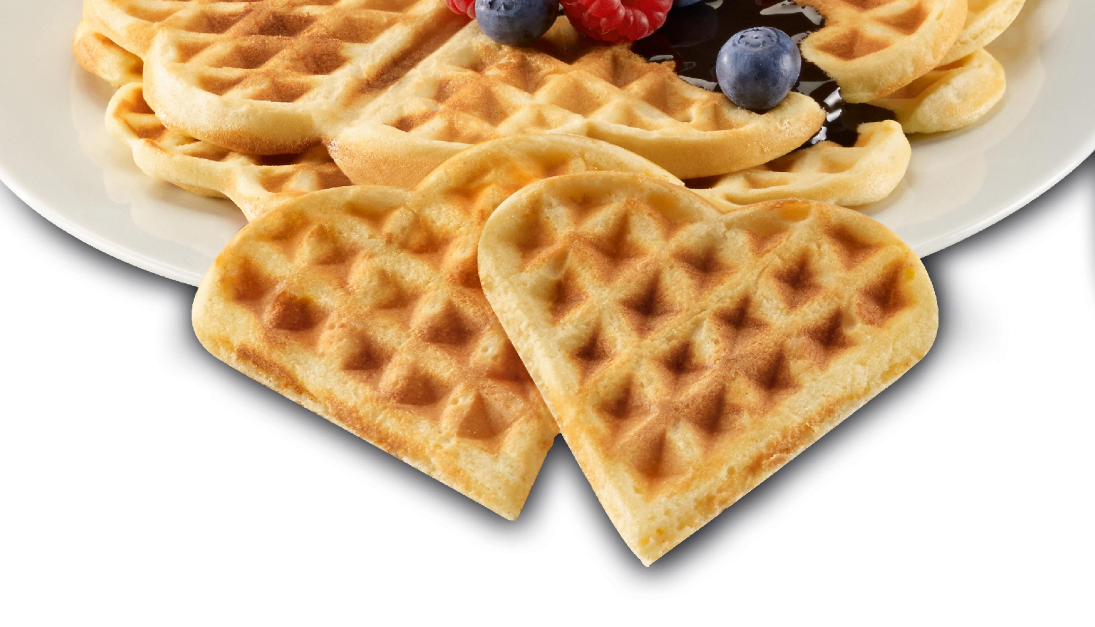 Herzförmige Waffeln auf einem weißen Teller, einige mit Blaubeeren und Himbeeren.