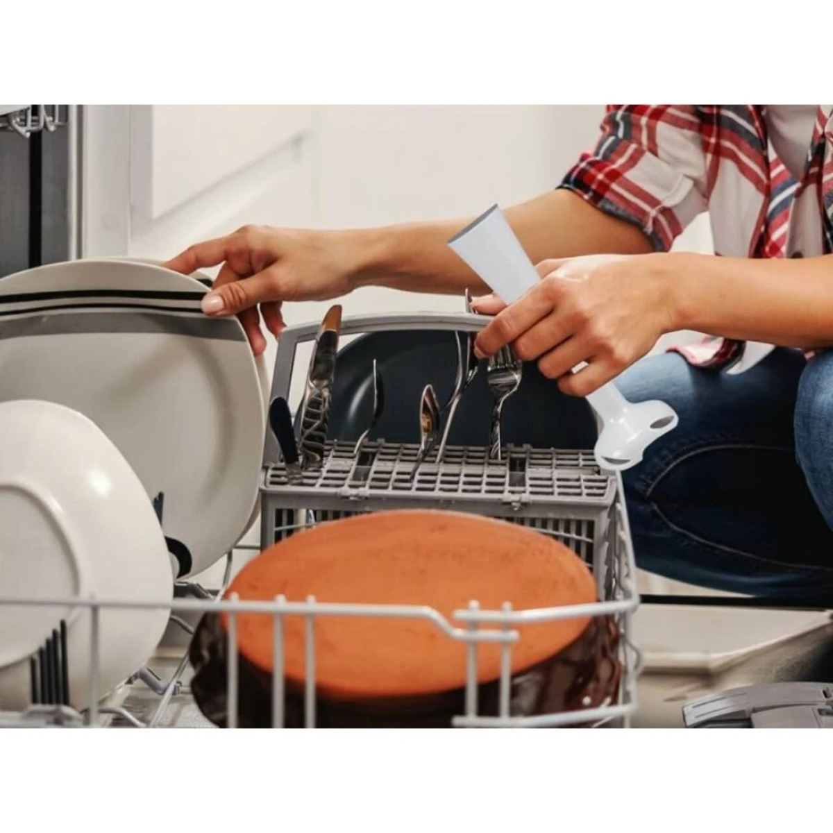 Osoba ładująca zmywarkę. Widoczne talerze, sztućce i kubek blendera.