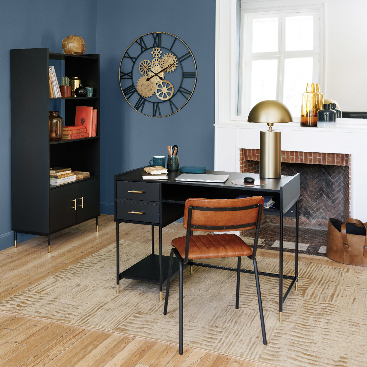 Pared azul con escritorio y silla negros. Hay un reloj, una estantería y una bolsa de cuero marrón.