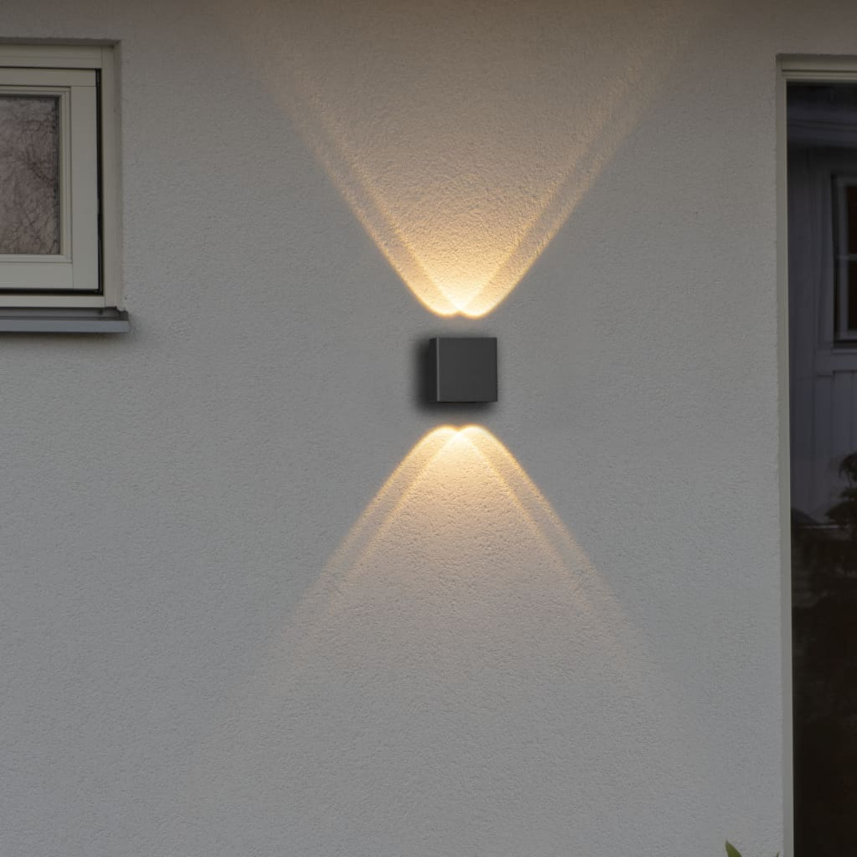 Eine quadratische Wandleuchte, die Licht nach oben und unten an einer weißen Wand ausstrahlt.
