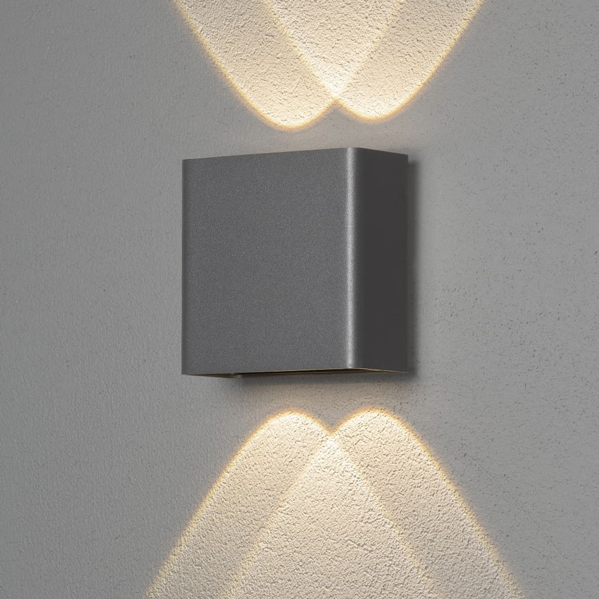 Quadratische graue Wandleuchte, die Licht nach oben und unten an einer grauen Wand emittiert.