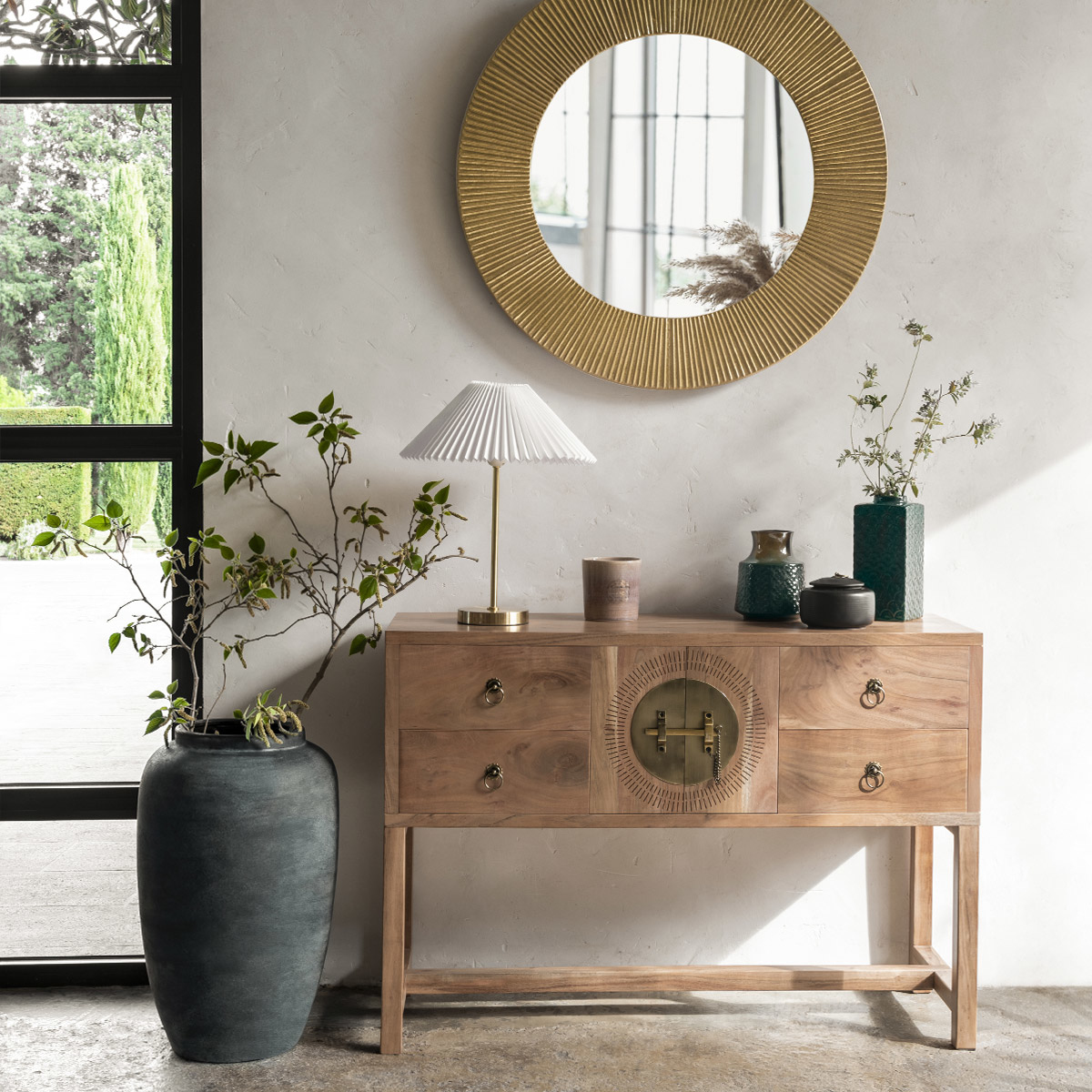 Gabinete de madera con espejo arriba, una lámpara y un jarrón con plantas, en una habitación.