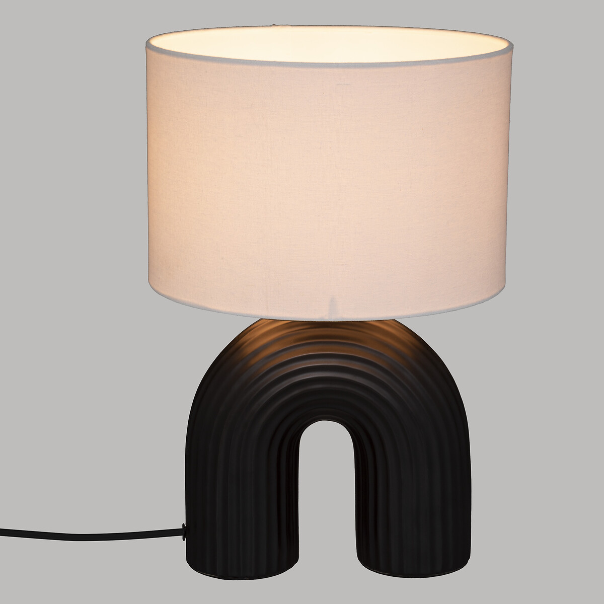 Una lámpara negra con base curva y pantalla cilíndrica blanca.