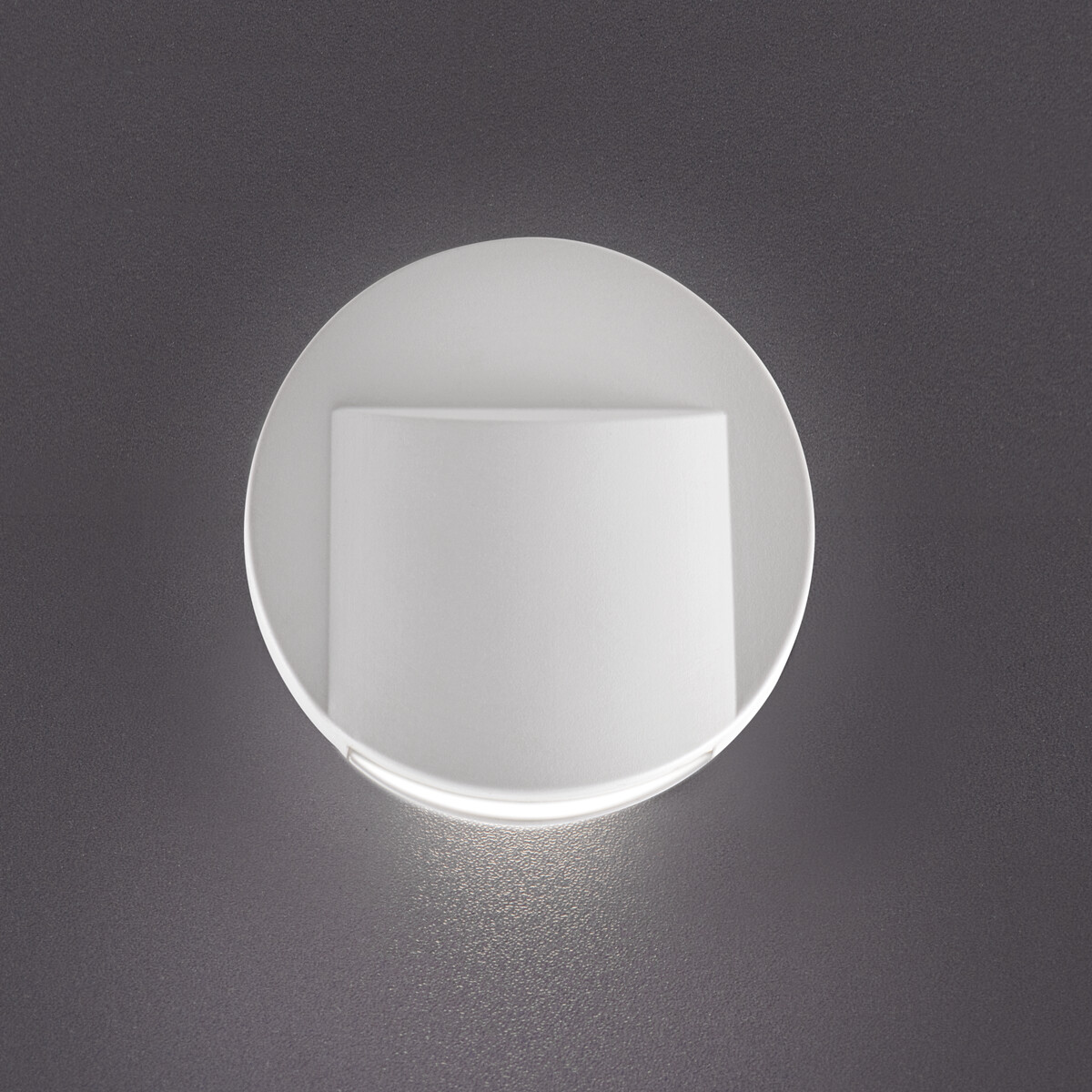 Una luz de pared circular blanca con una fuente de luz rectangular empotrada. Pared gris.