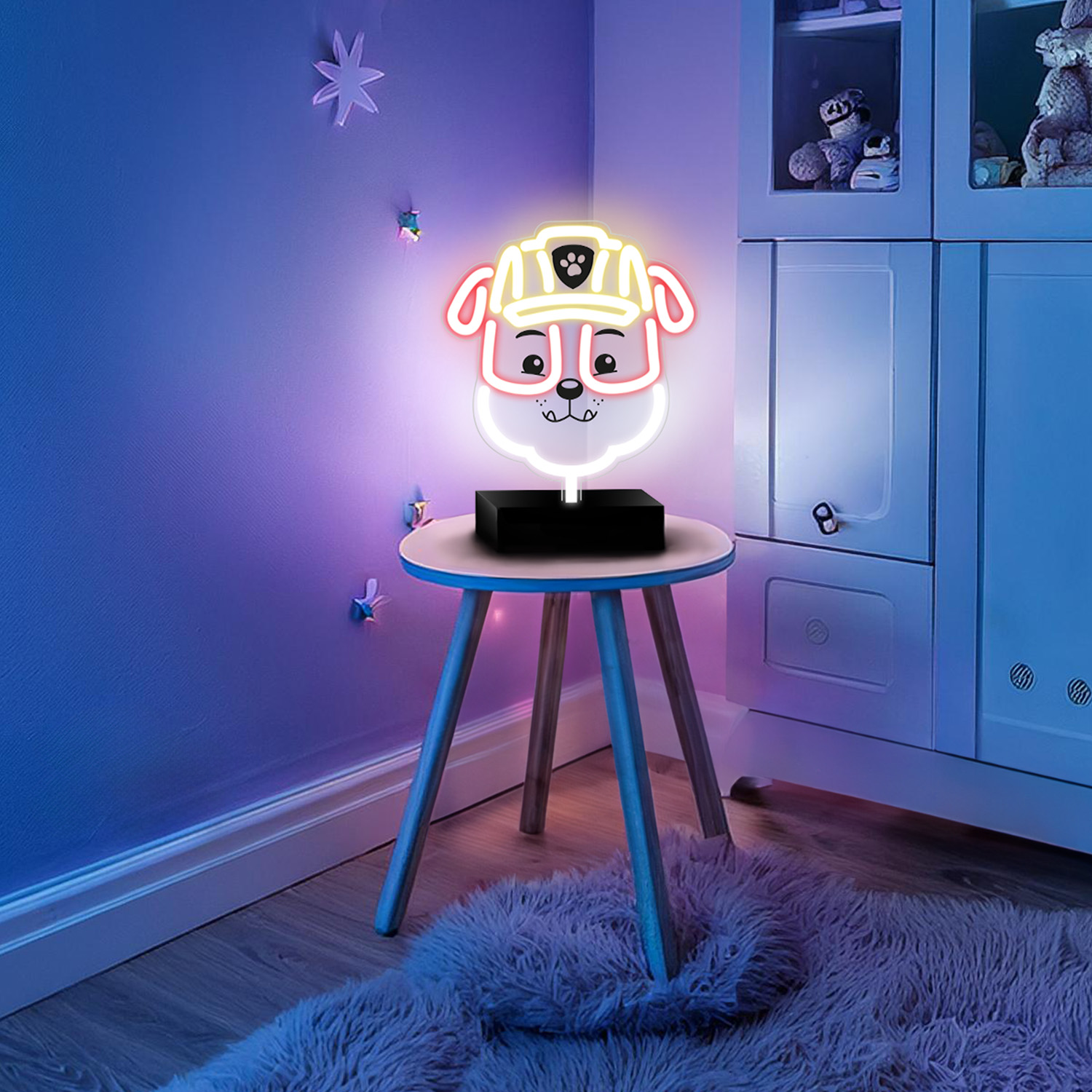 Neonowa lampa w kształcie psa na małym stoliku z puszystym dywanem. Niebieska ściana, zabawki i biała półka.