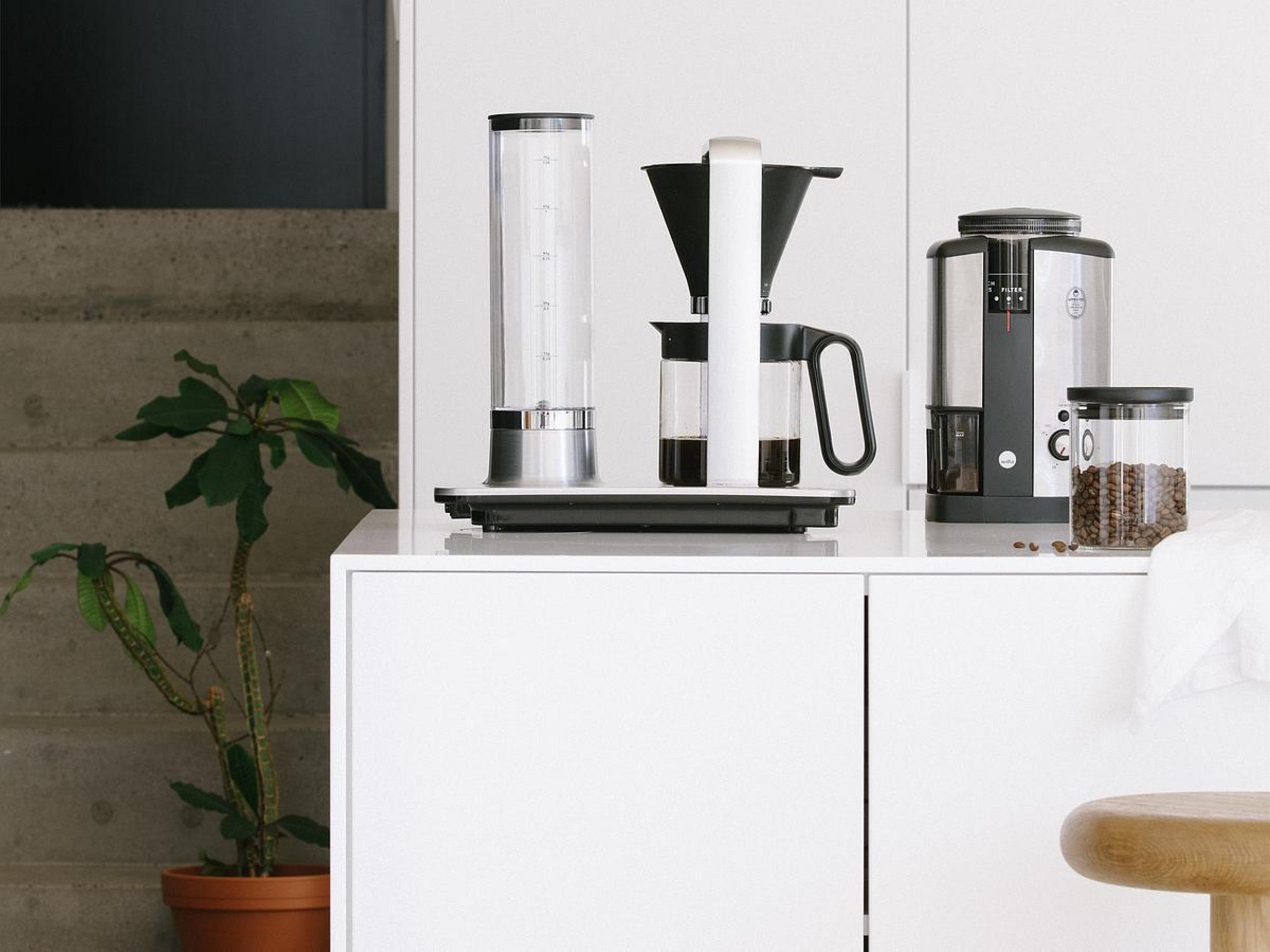 Kaffeemaschineneinrichtung mit hohem Wasserbehälter, Filter und Kaffeebbehälter auf weißer Oberfläche.