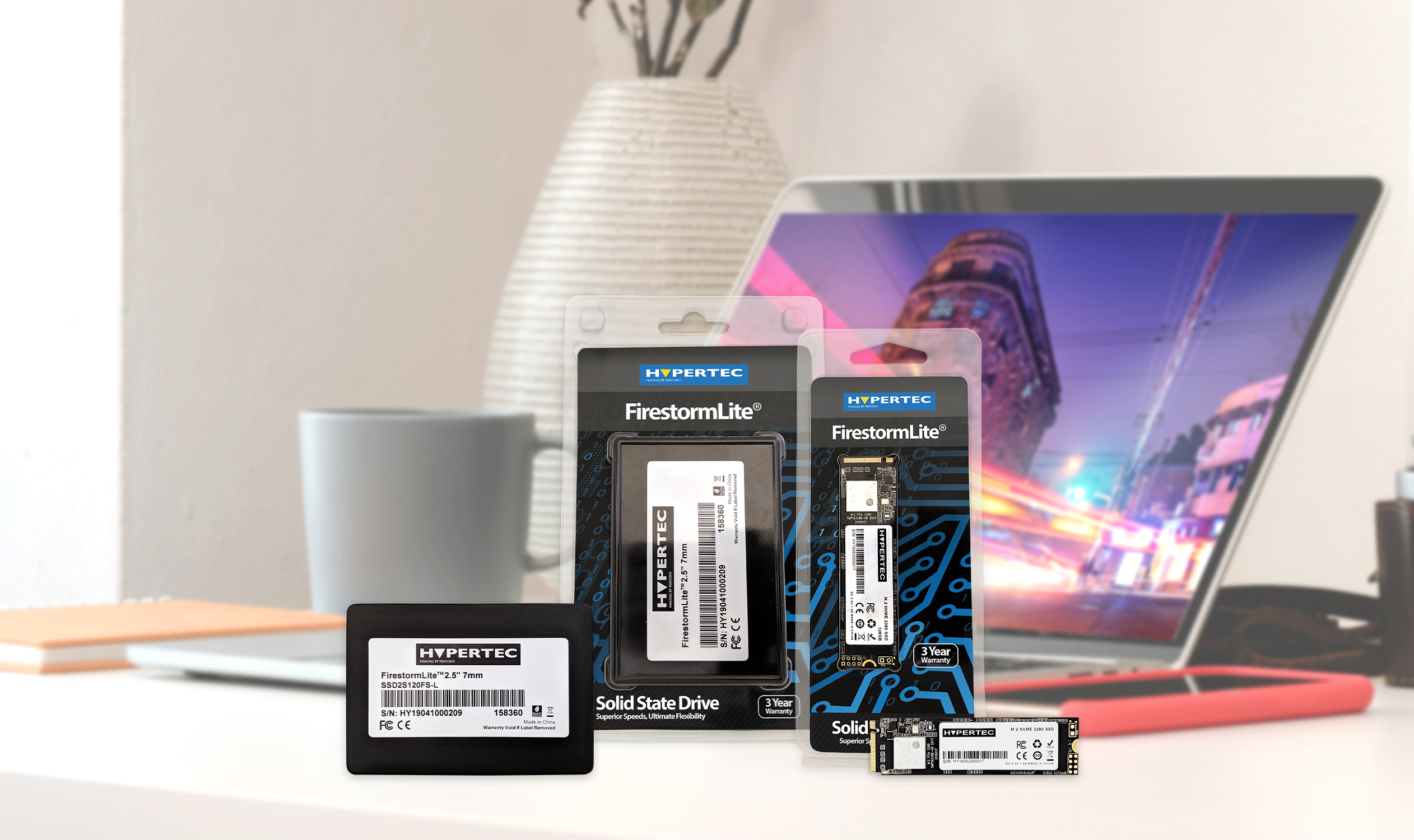 Una scrivania con più SSD, confezioni e un laptop. Lo sfondo è sfocato.