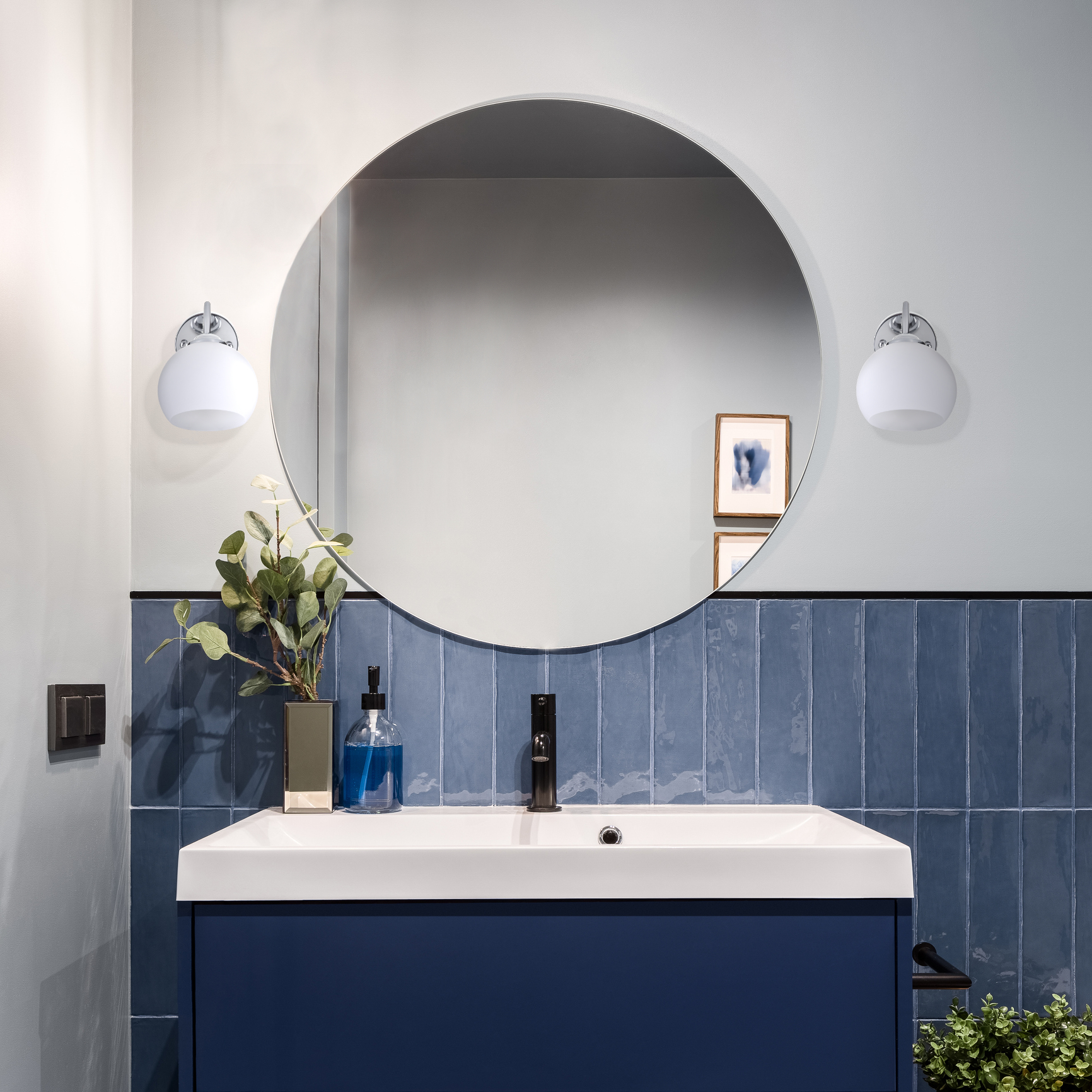 Lavandino del bagno con specchio. Specchio rotondo sopra un mobile blu, con luci e dispenser di sapone.