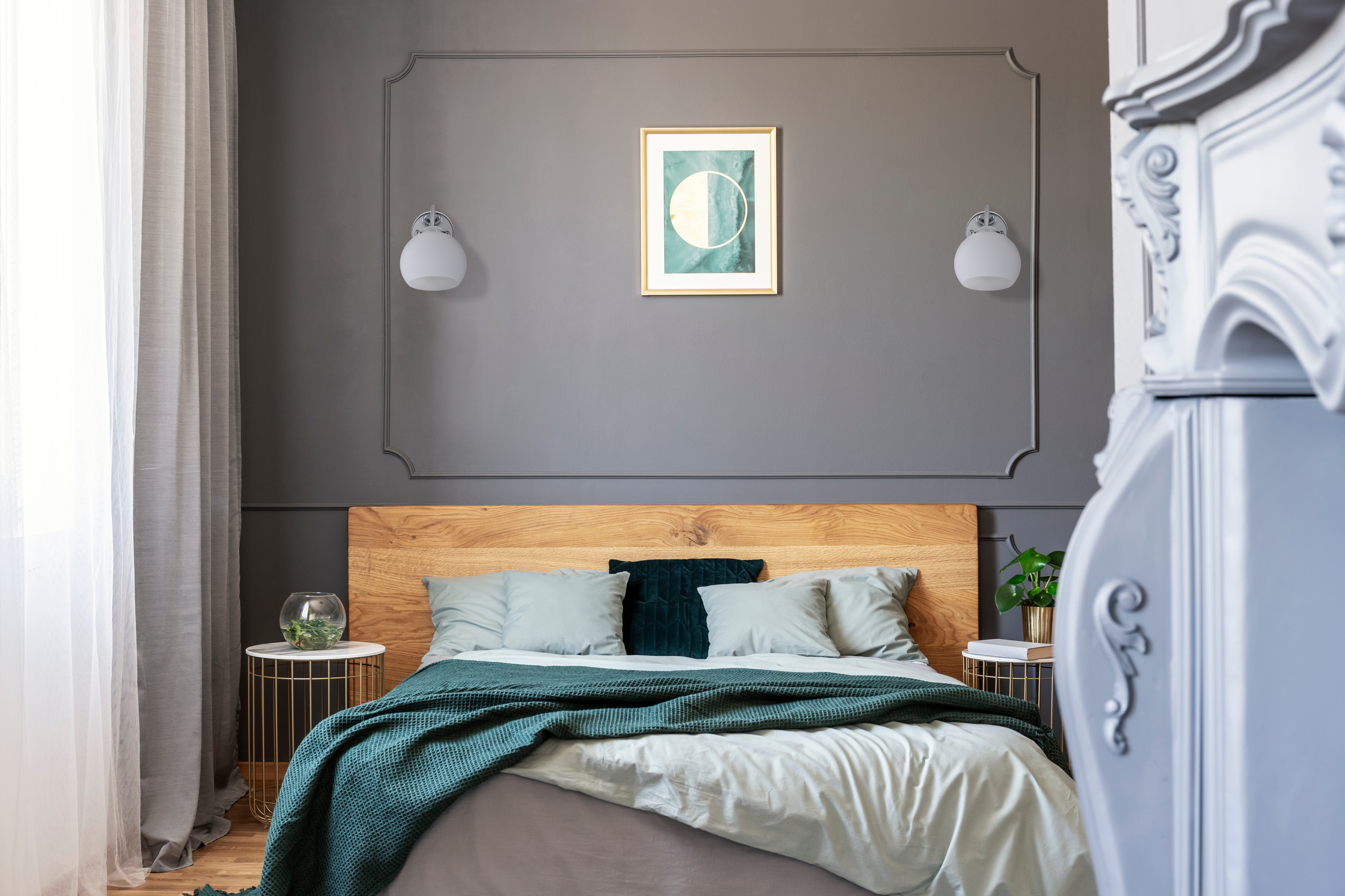Camera da letto con pareti grigie, testiera in legno e letto con accenti verdi. Due lampade e un quadro sulla parete.