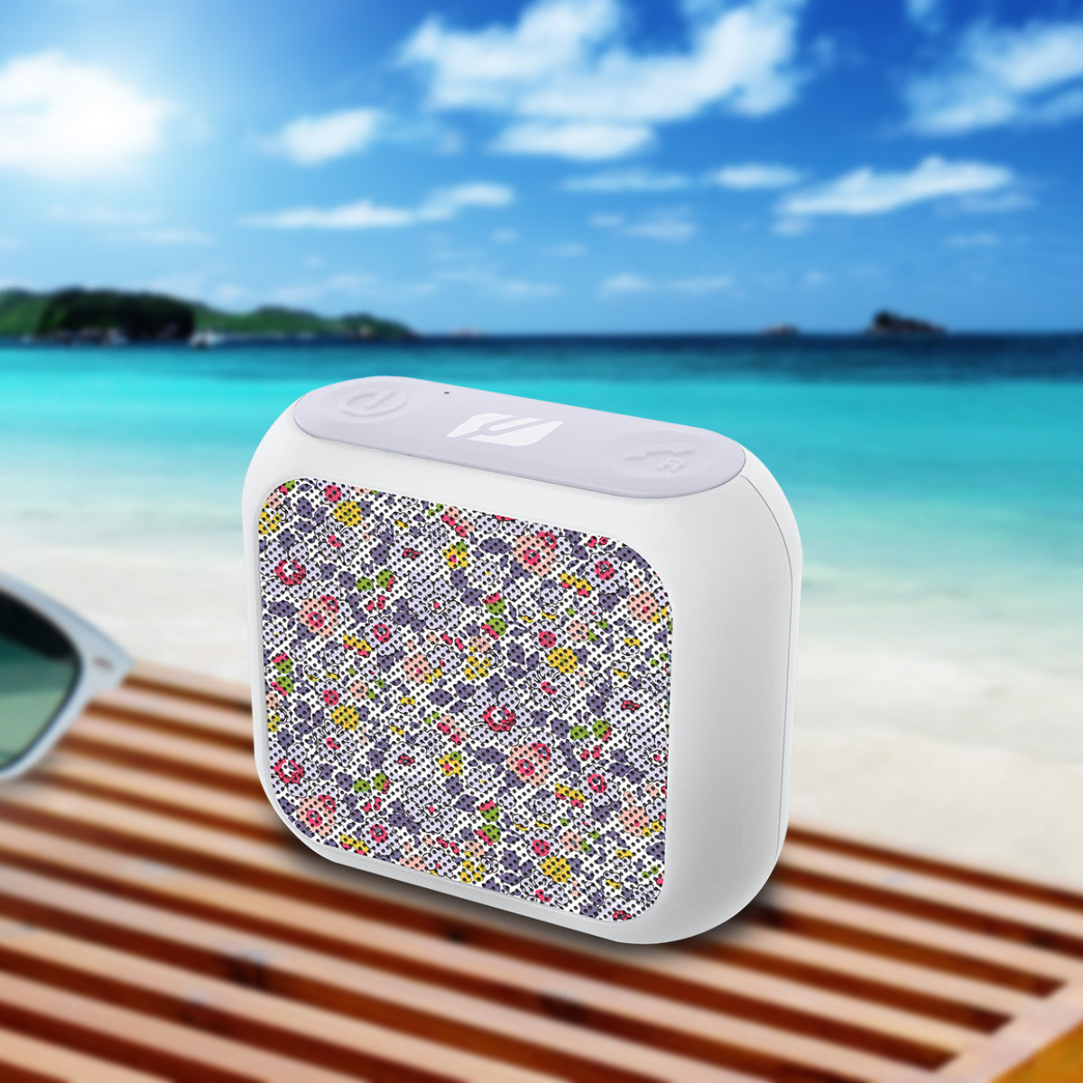 Un haut-parleur blanc avec un motif coloré, sur une surface en bois près de la plage.