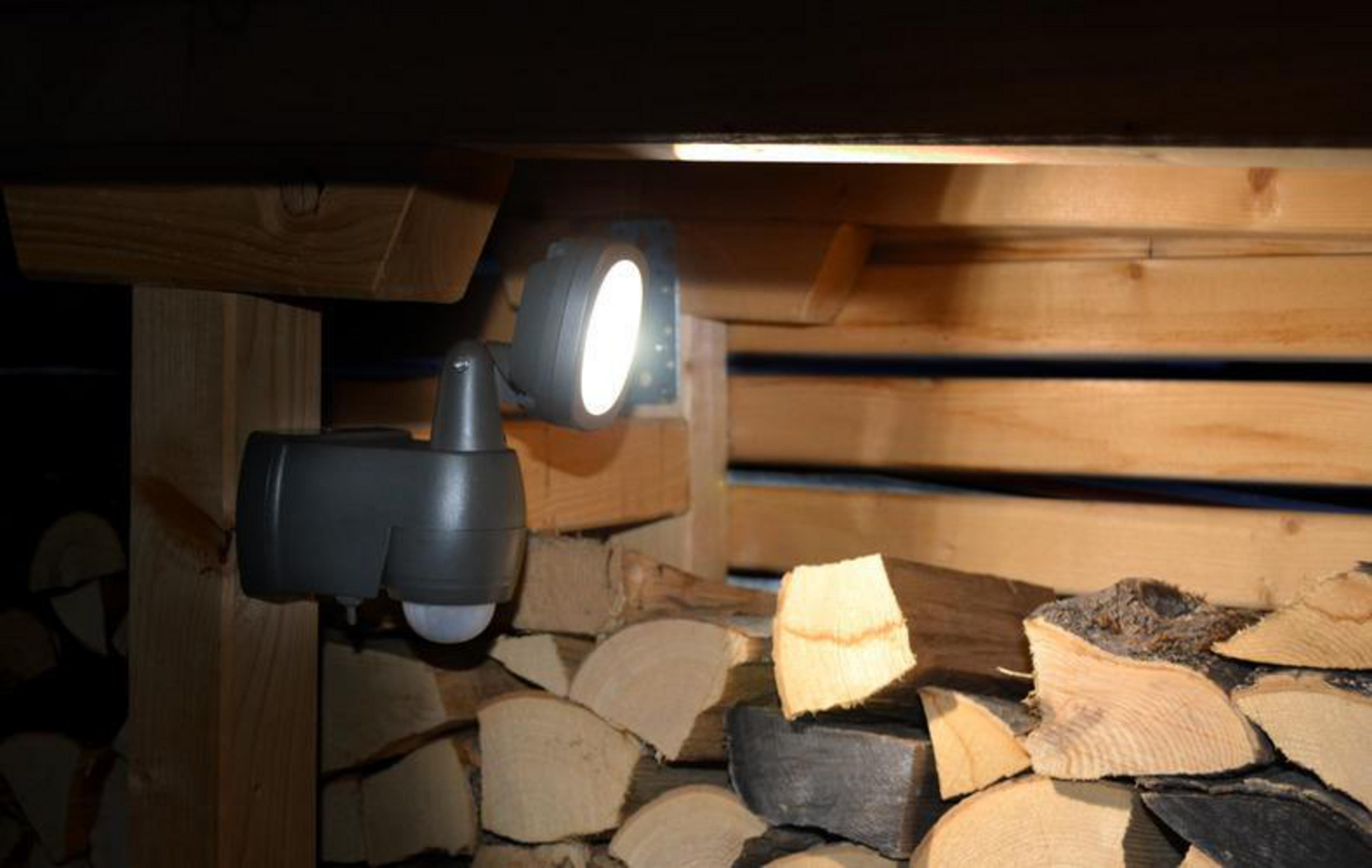 Reflektor pod drewnianą konstrukcją. Światło pada na drewno i stos kłód.