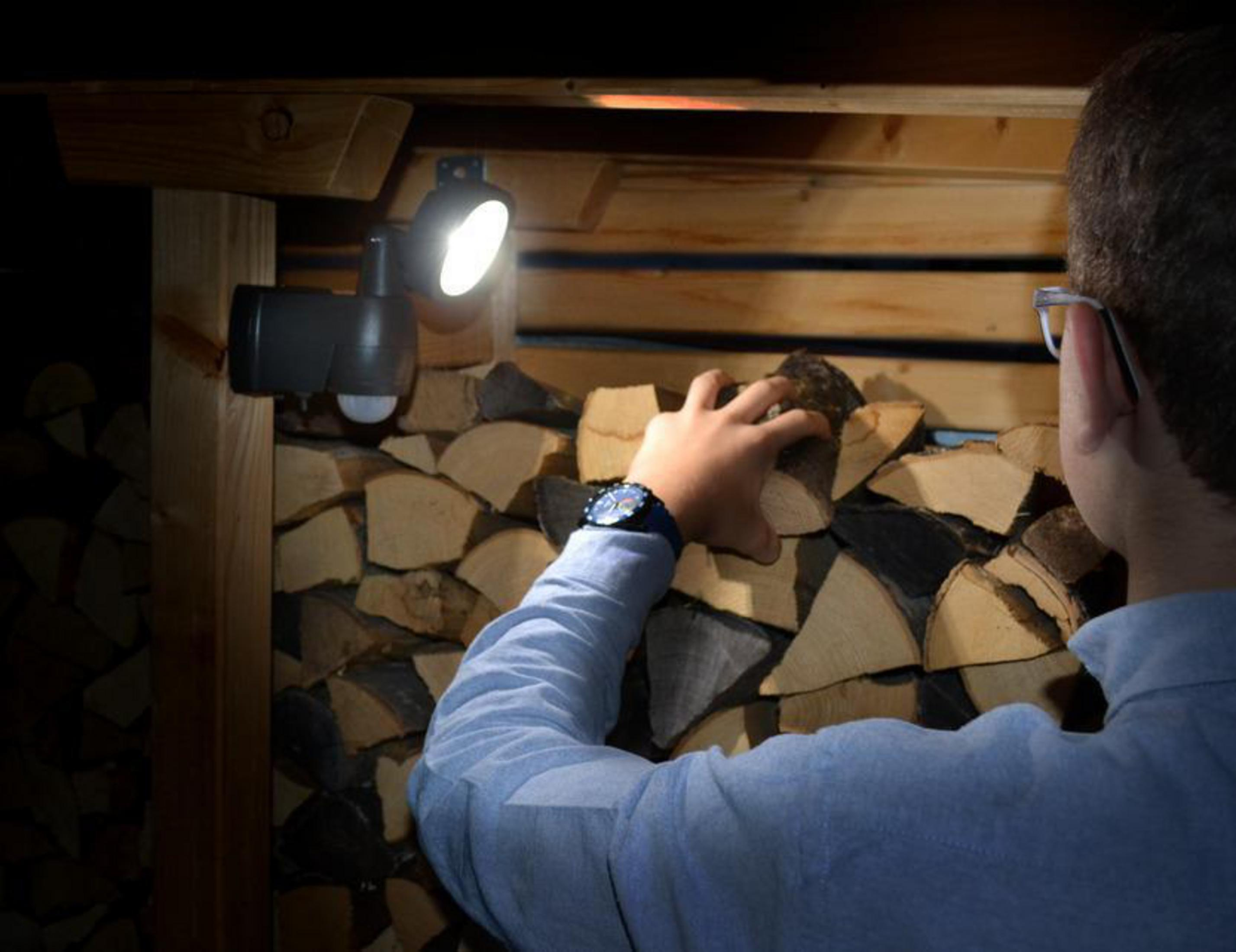 Osoba układająca drewno opałowe obok oprawy oświetleniowej z czujnikiem ruchu.