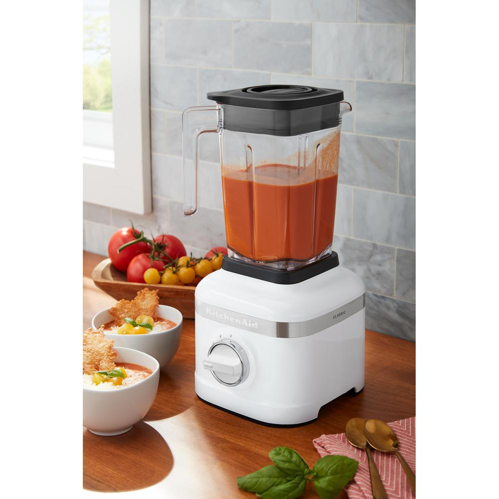 Un frullatore KitchenAid bianco con zuppa di pomodoro rossa in un contenitore trasparente.
