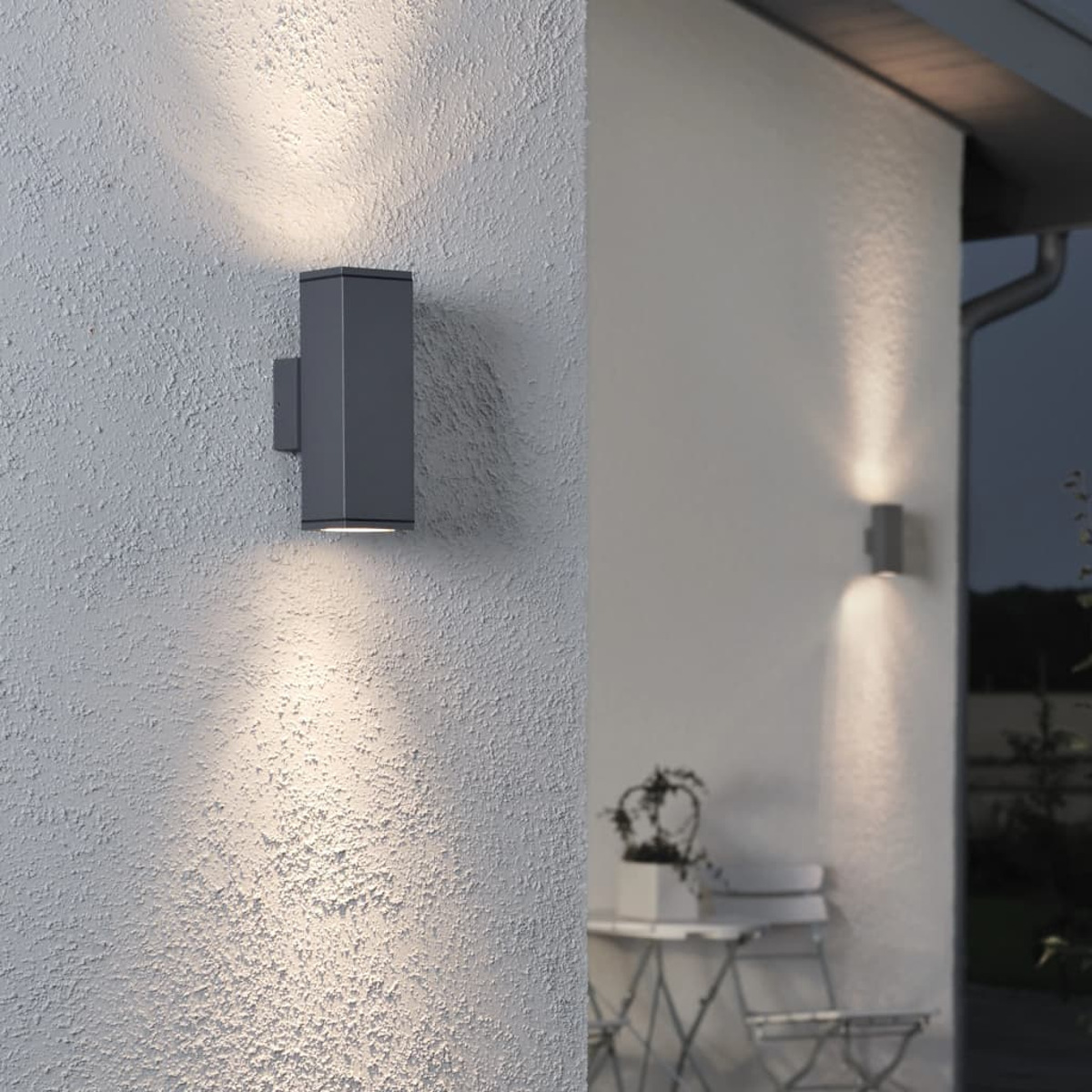 Una lampada da parete esterna installata su un muro strutturato, con luce simile sullo sfondo al tramonto.