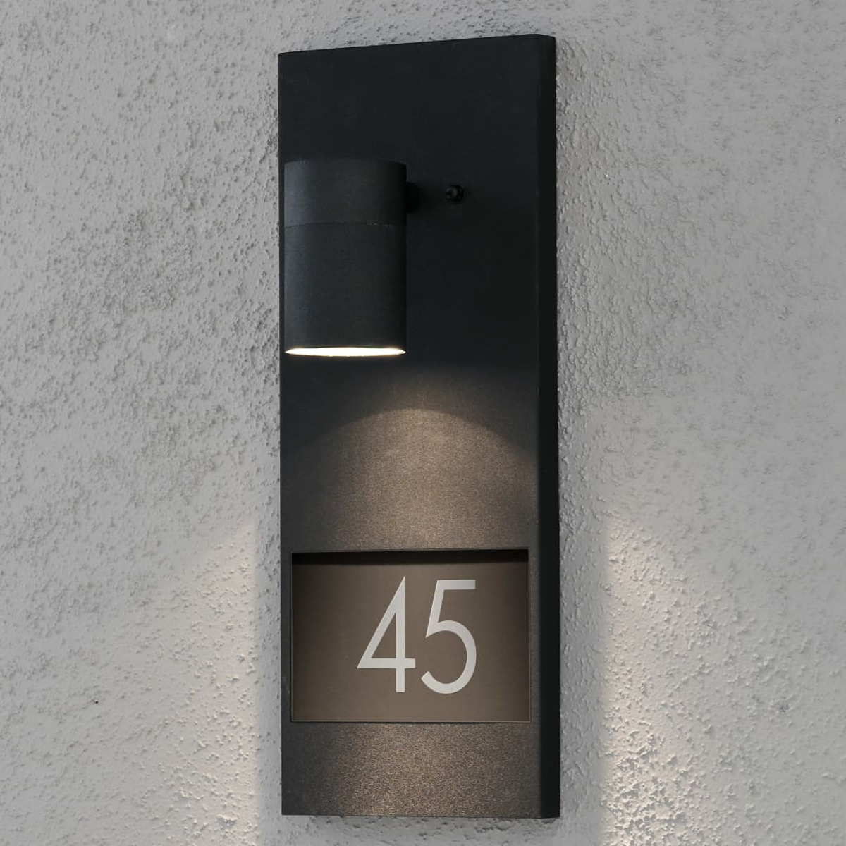 Luce nera a parete con numero 45 e lampada cilindrica sopra. Il muro è strutturato.