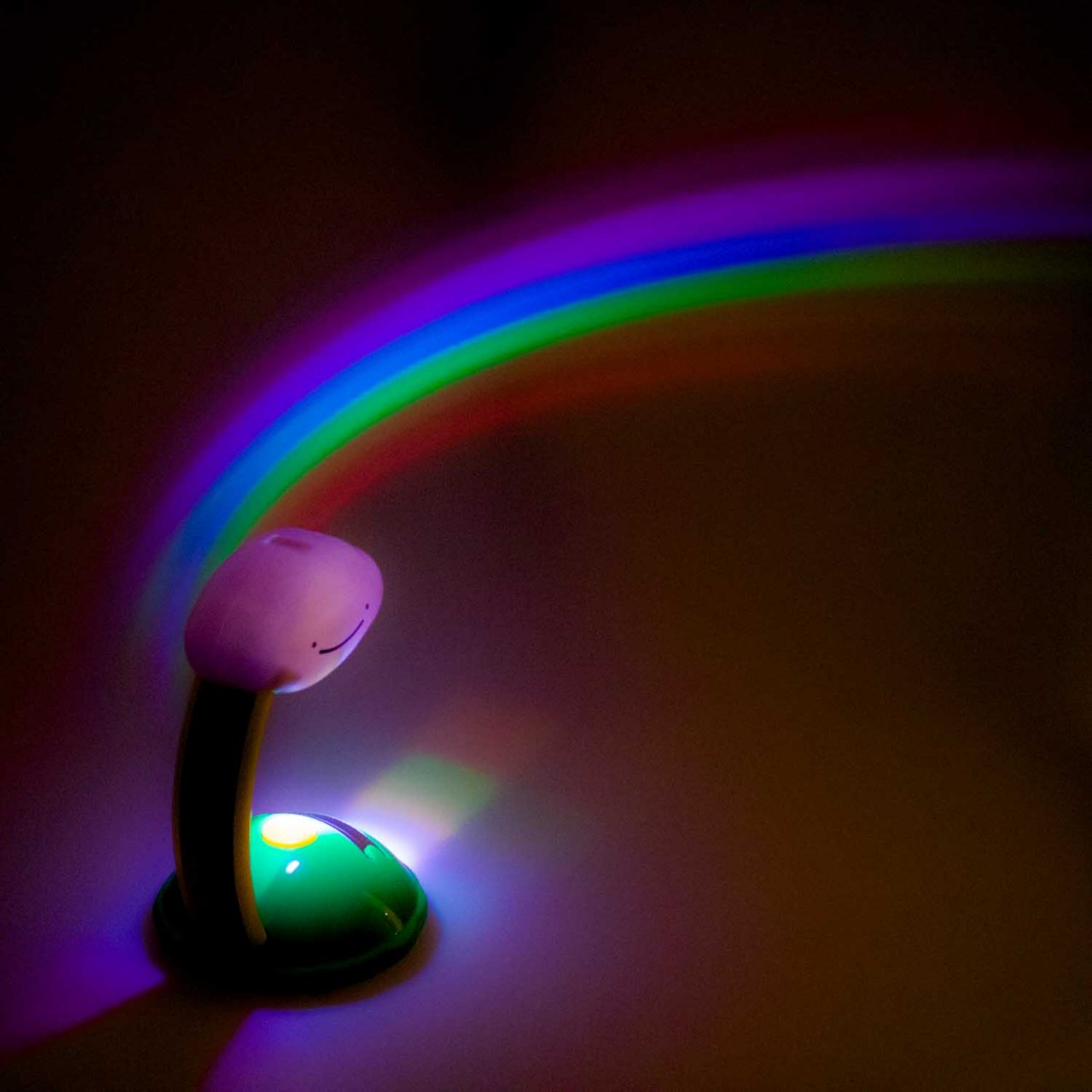 Lampe mit Regenbogenprojektion. Grüne Basis, Cartoon-Stil. Dunkler Hintergrund.
