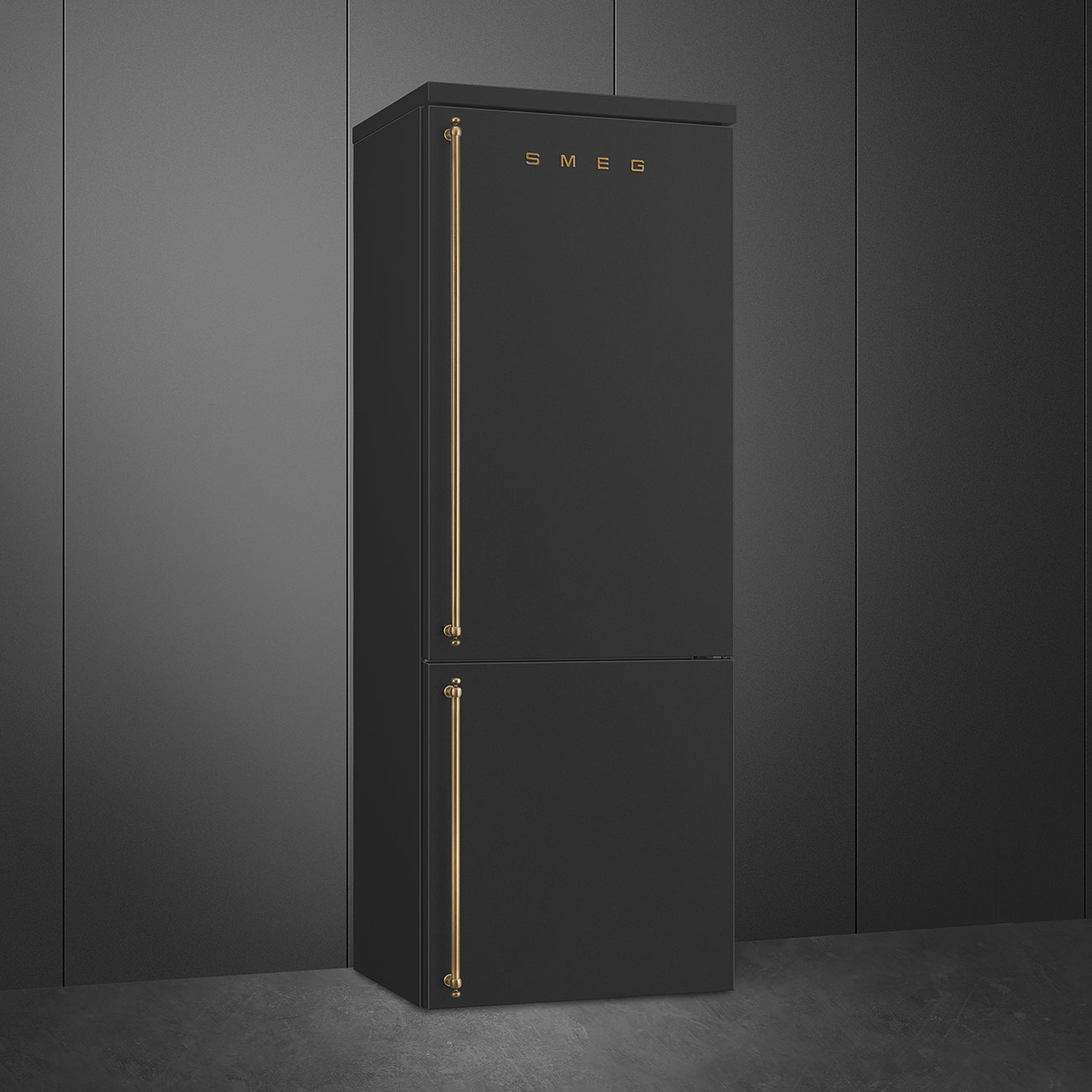 Frigorifero Smeg nero con maniglie dorate, in piedi contro un muro grigio e pavimento in cemento.